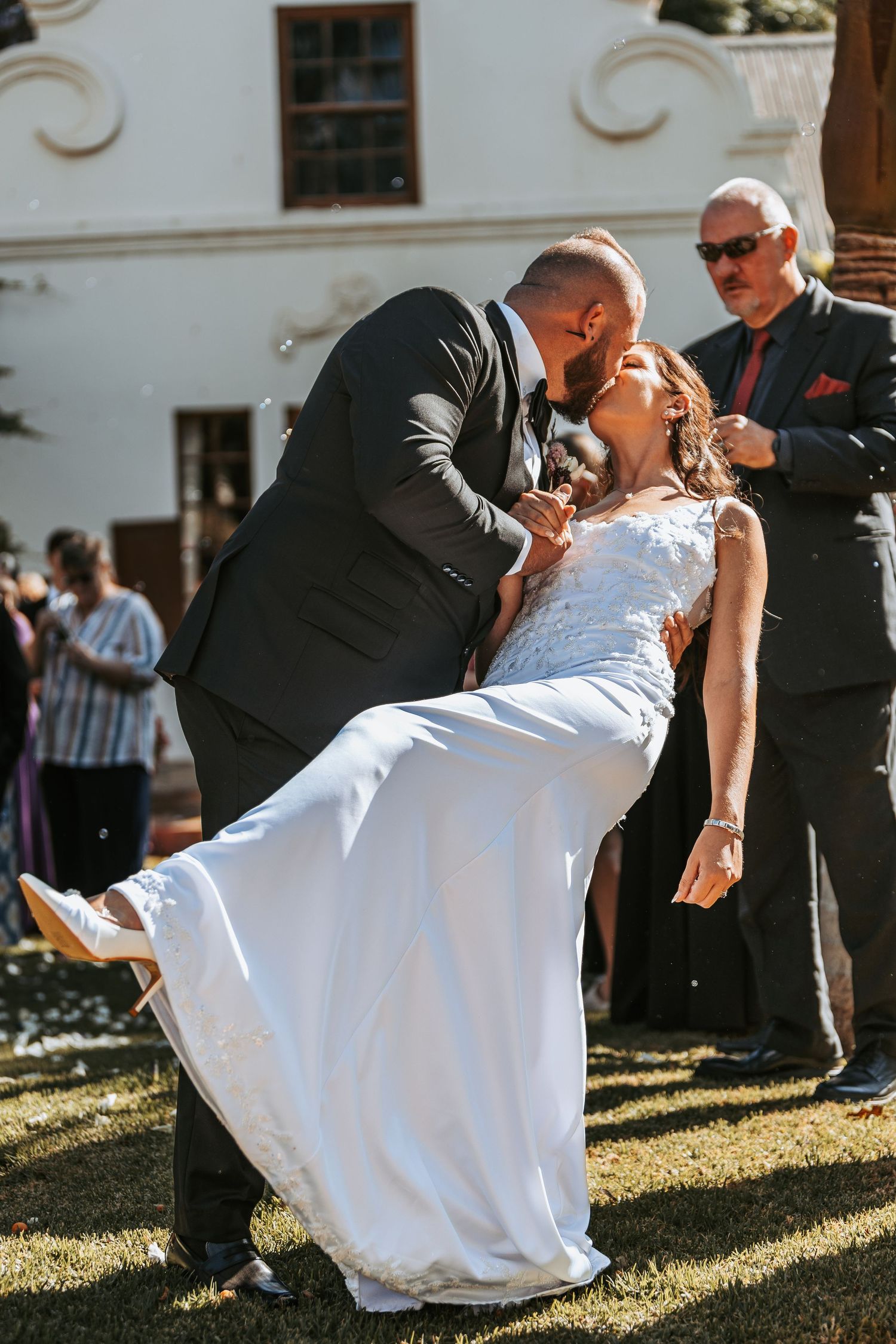 Groom dips bride in white dress during romantic outdoor wedding moment.