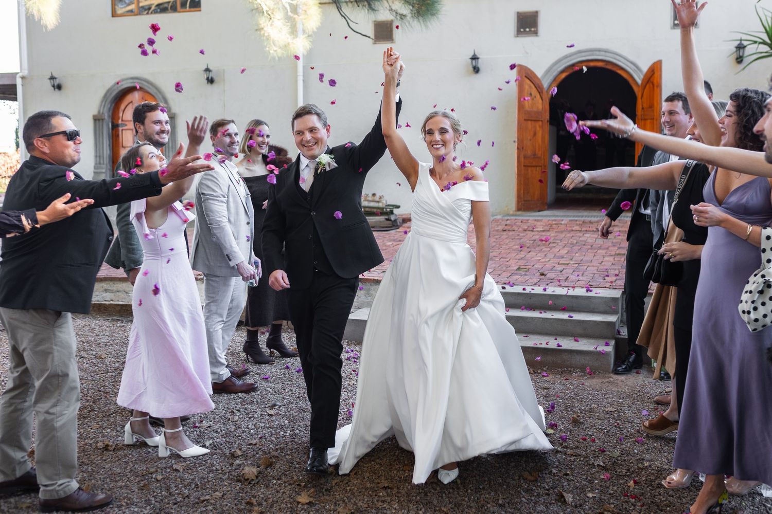 Newlyweds celebrating with guests tossing confetti outside church after wedding ceremony.