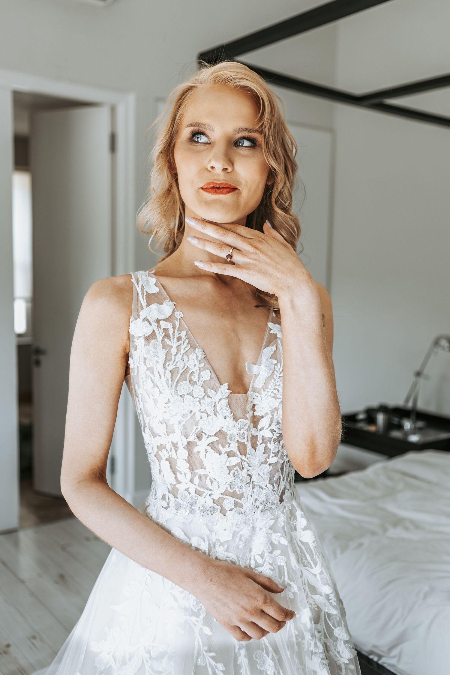 Elegant bride in lace wedding gown with flowing train poses in a bright modern room.