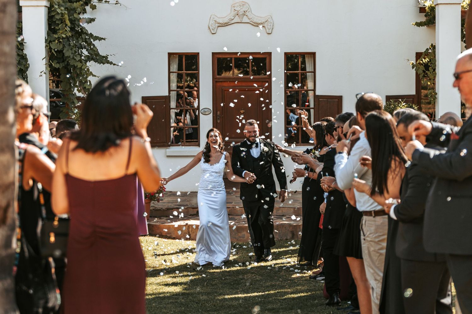 Wedding guests mingle outside white building during outdoor reception.