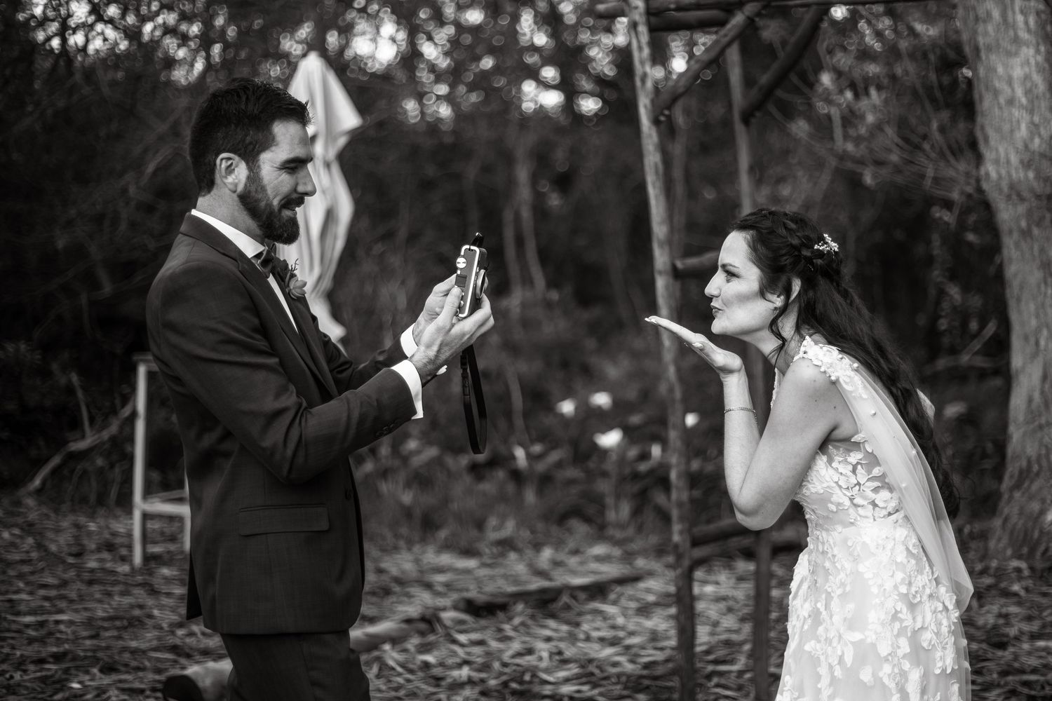 A couple in wedding attire poses together in a forest setting for a romantic photoshoot.