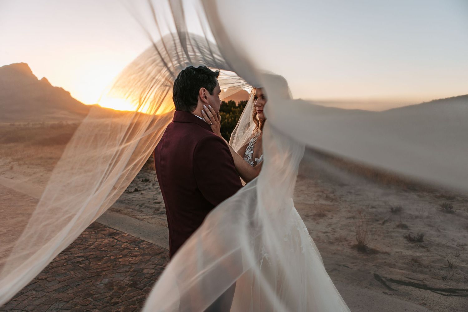 A romantic wedding photo captured at golden hour in a desert landscape.