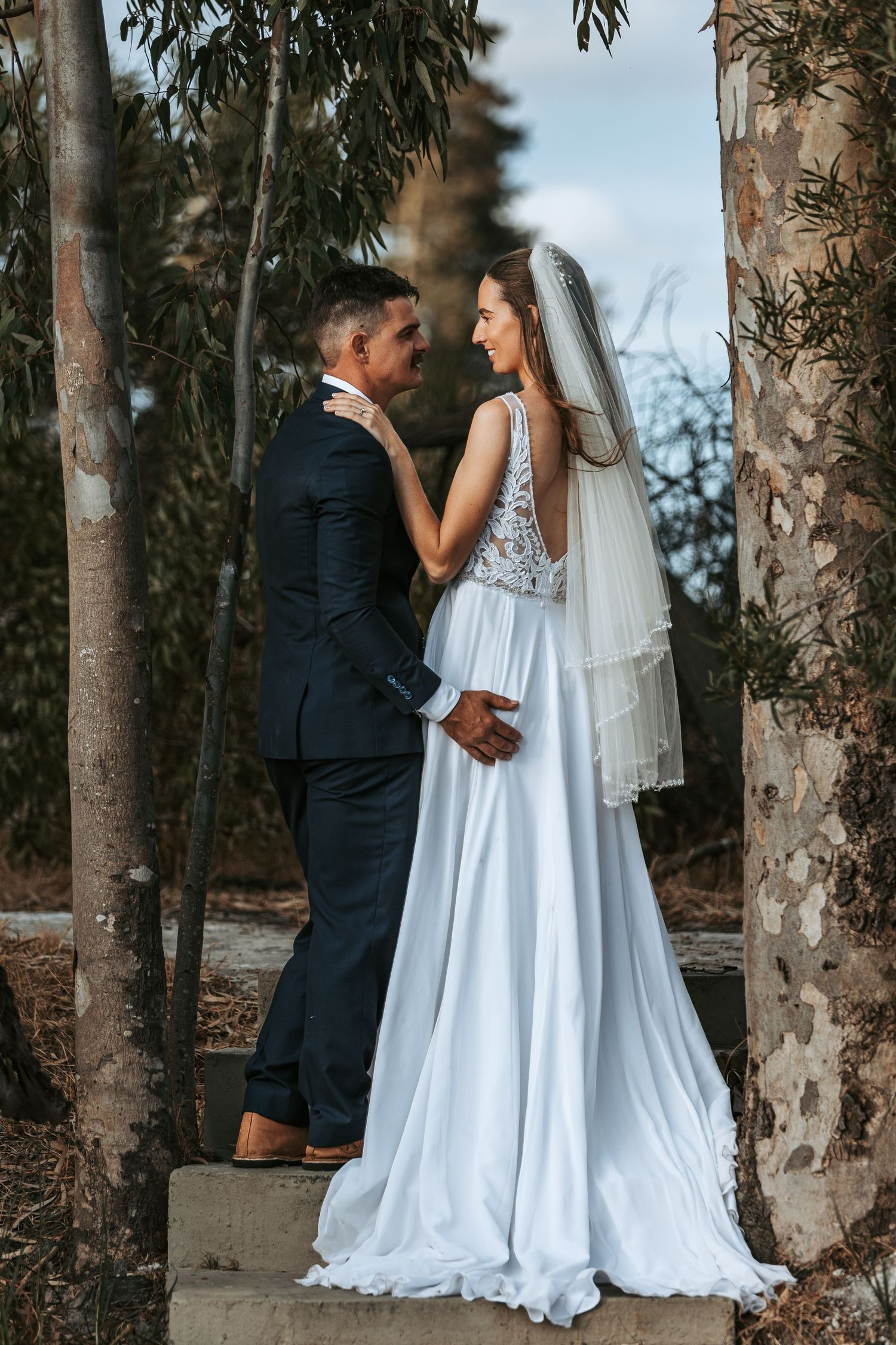 Wedding couple shares intimate moment among eucalyptus trees in outdoor setting.