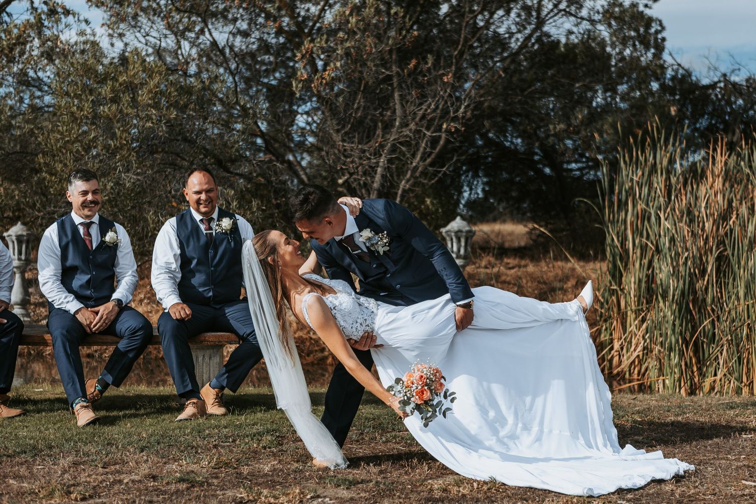 Wedding couple poses playfully on grass during their outdoor photo session.