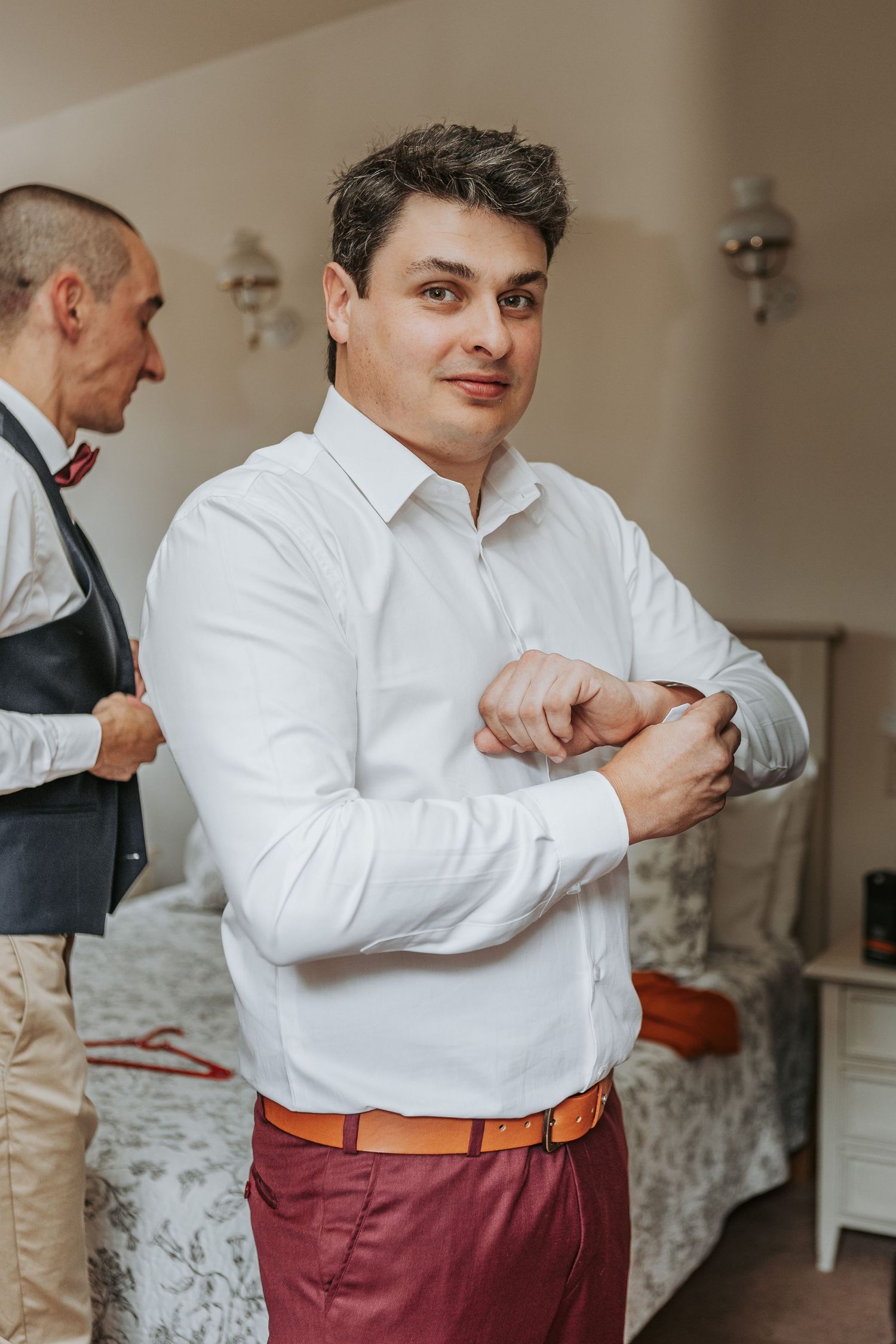 Person in white dress shirt and burgundy pants adjusting sleeves while getting ready.