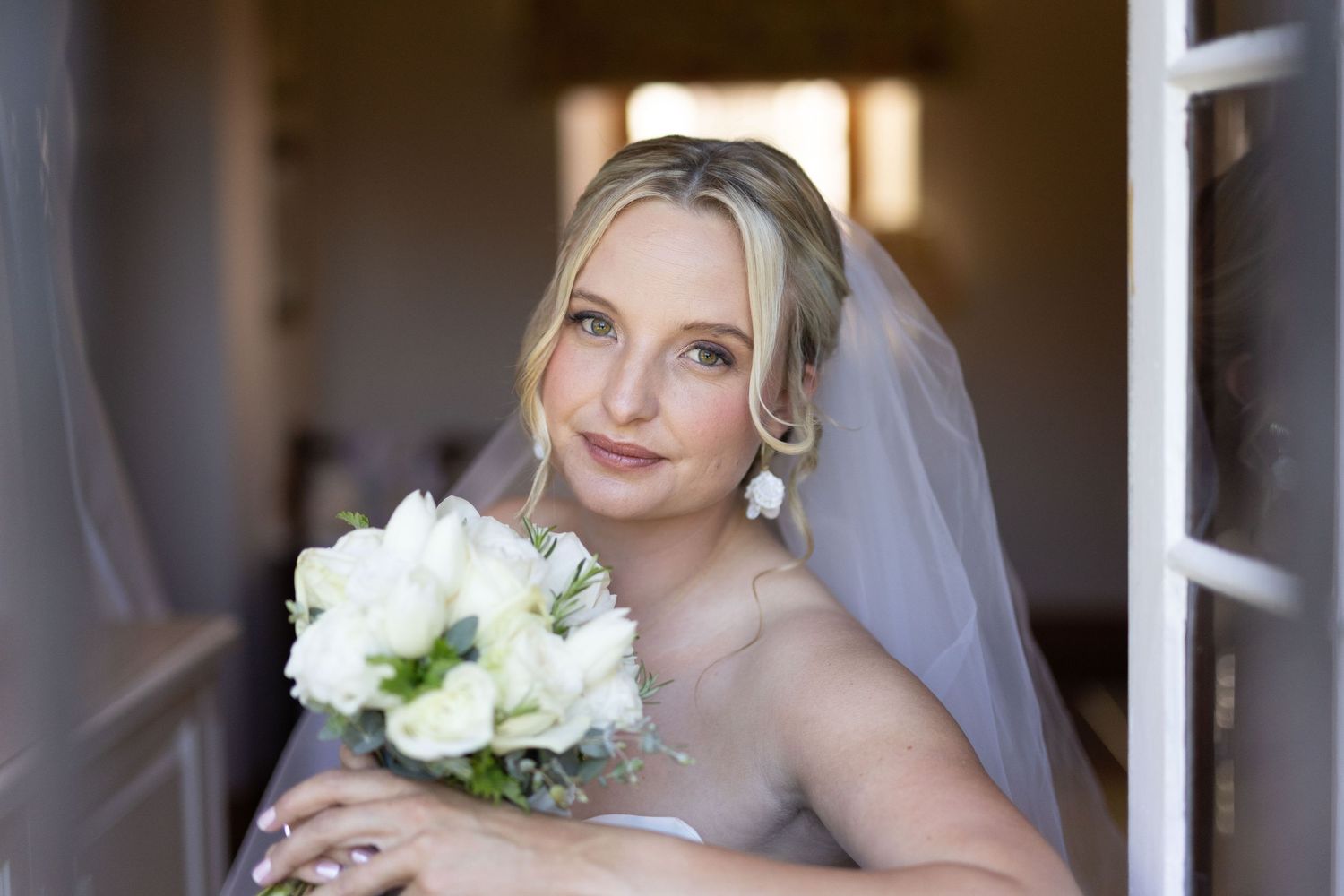 Bride in classic white gown and veil poses for bridal portraits with natural window lighting.