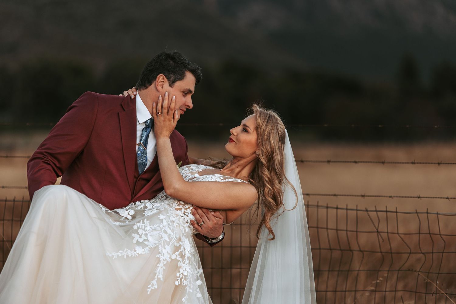 Playful wedding portrait of couple by rustic fence at sunset.