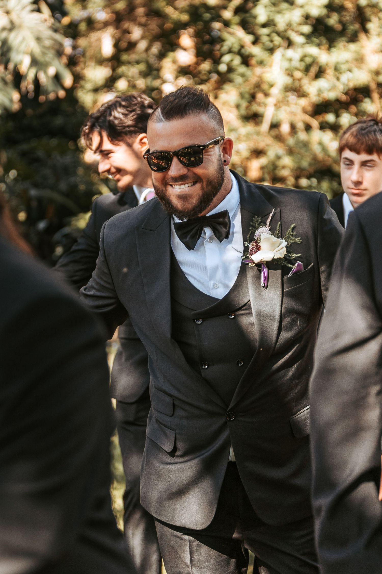 Groomsmen in black suits and bowties sharing laughs during outdoor wedding photos.