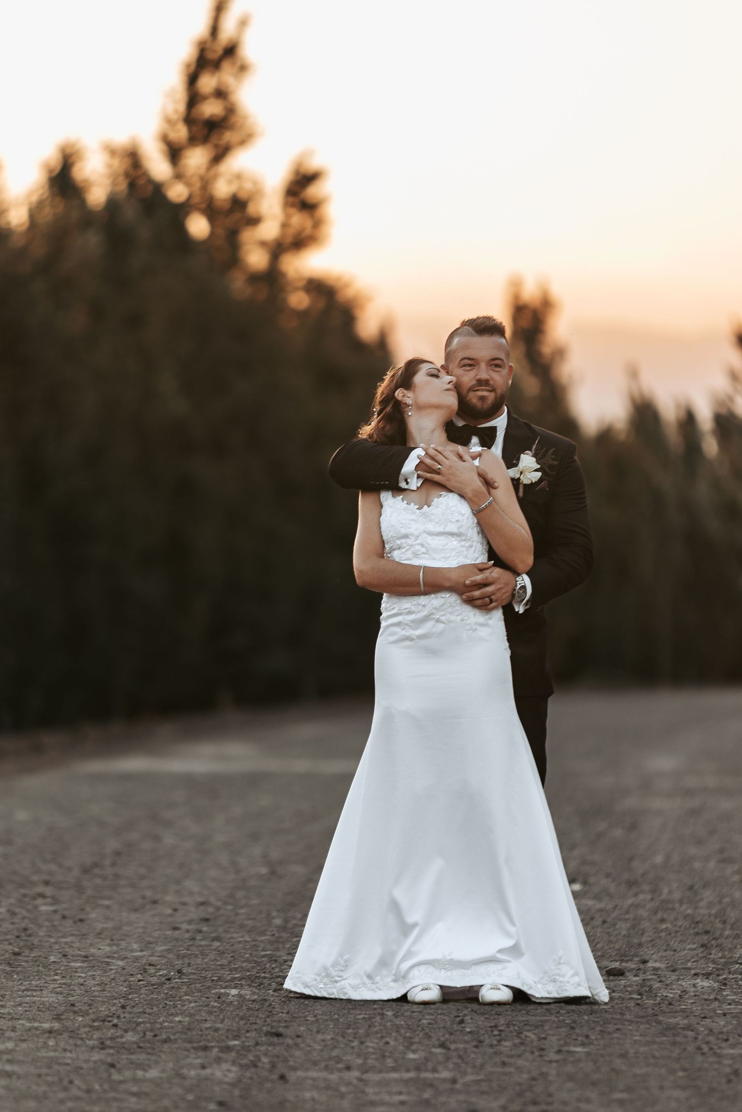 Wedding couple embracing on a desert path during sunset.