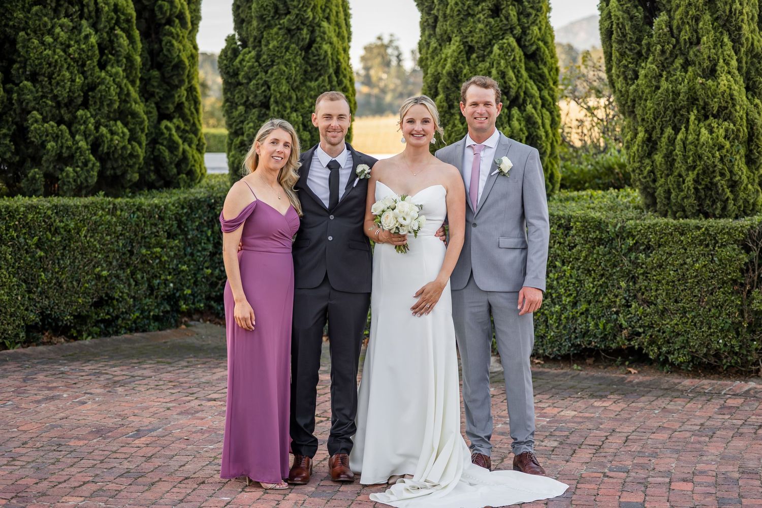 Wedding party members celebrate outdoors with cypress trees in the background.