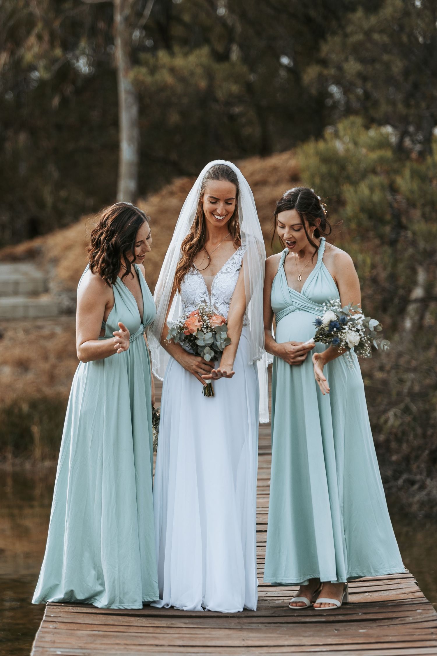 Bridesmaids in mint green dresses gather around bride in white gown on wooden deck.
