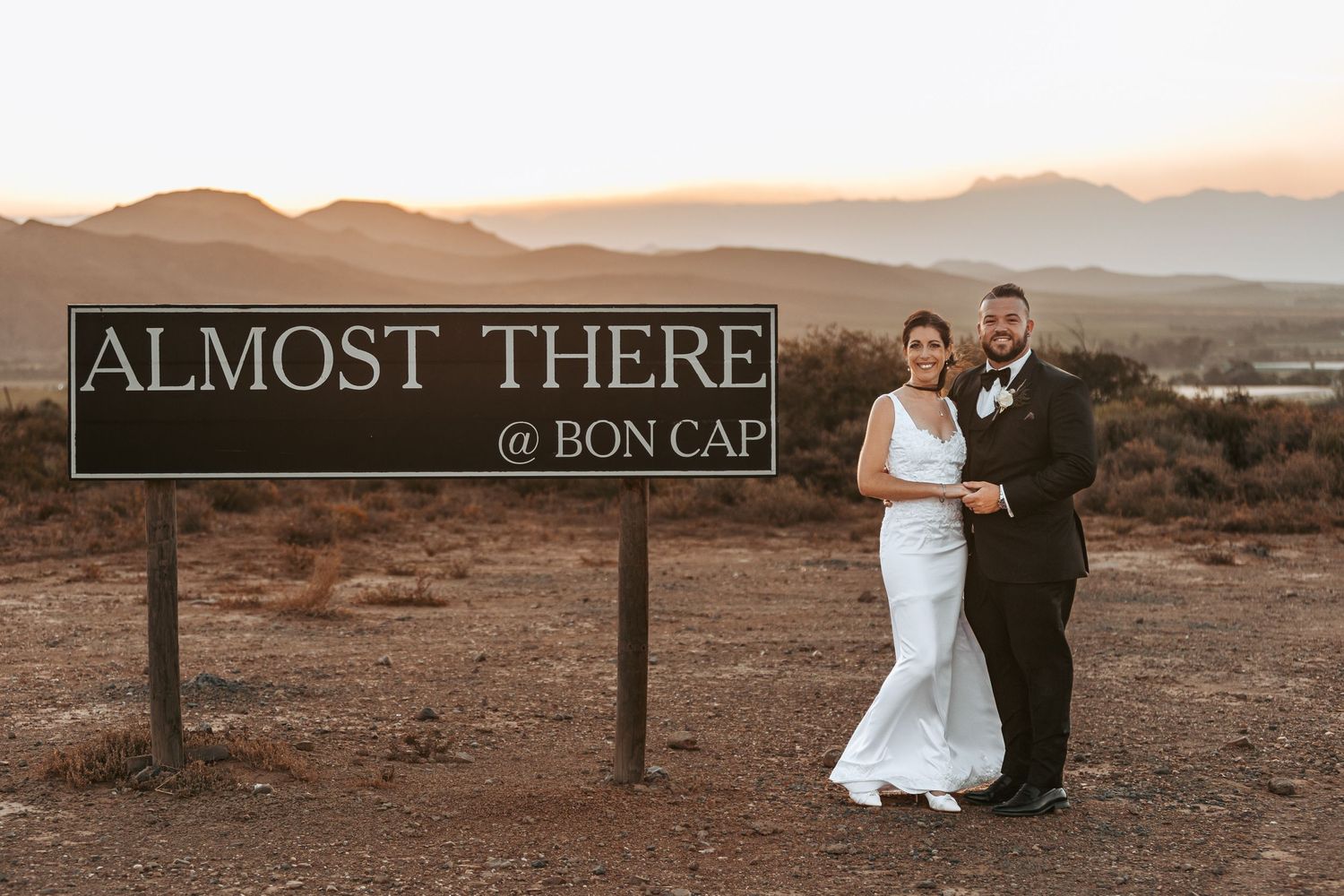 Wedding photos with 'Almost There' sign in desert landscape at sunset.