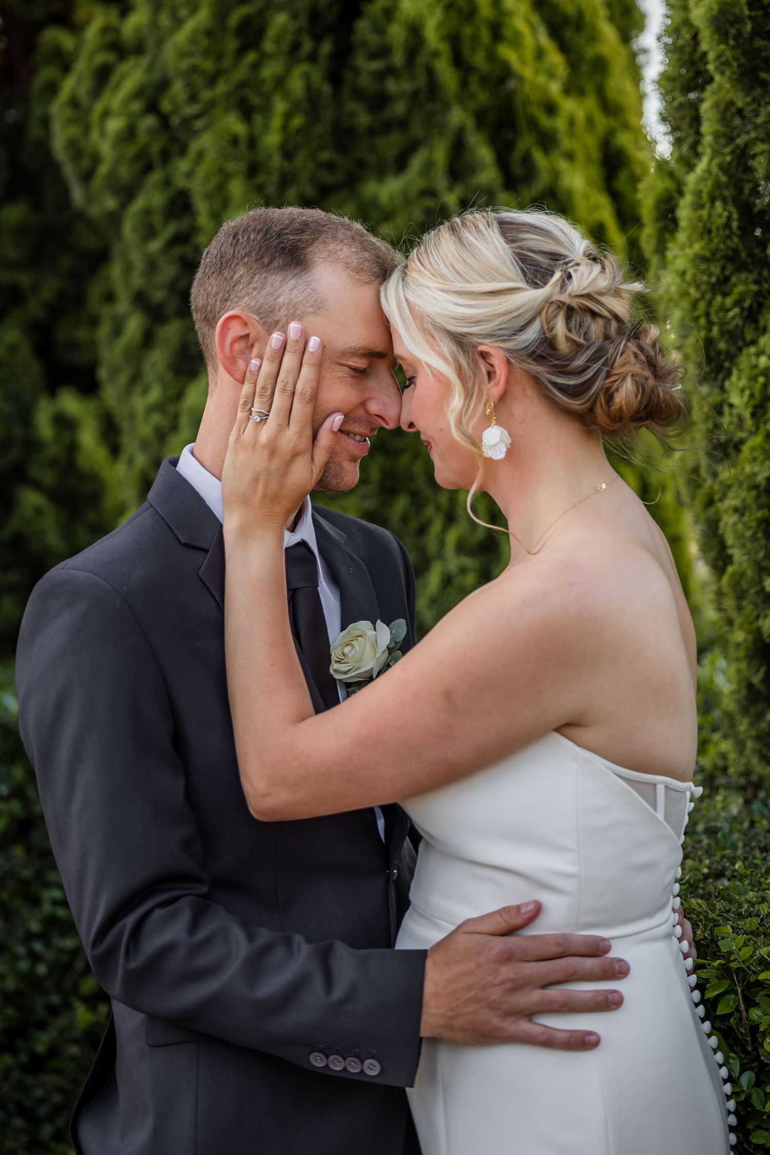 Intimate wedding couple portraits among green cypress trees showing tender moments.