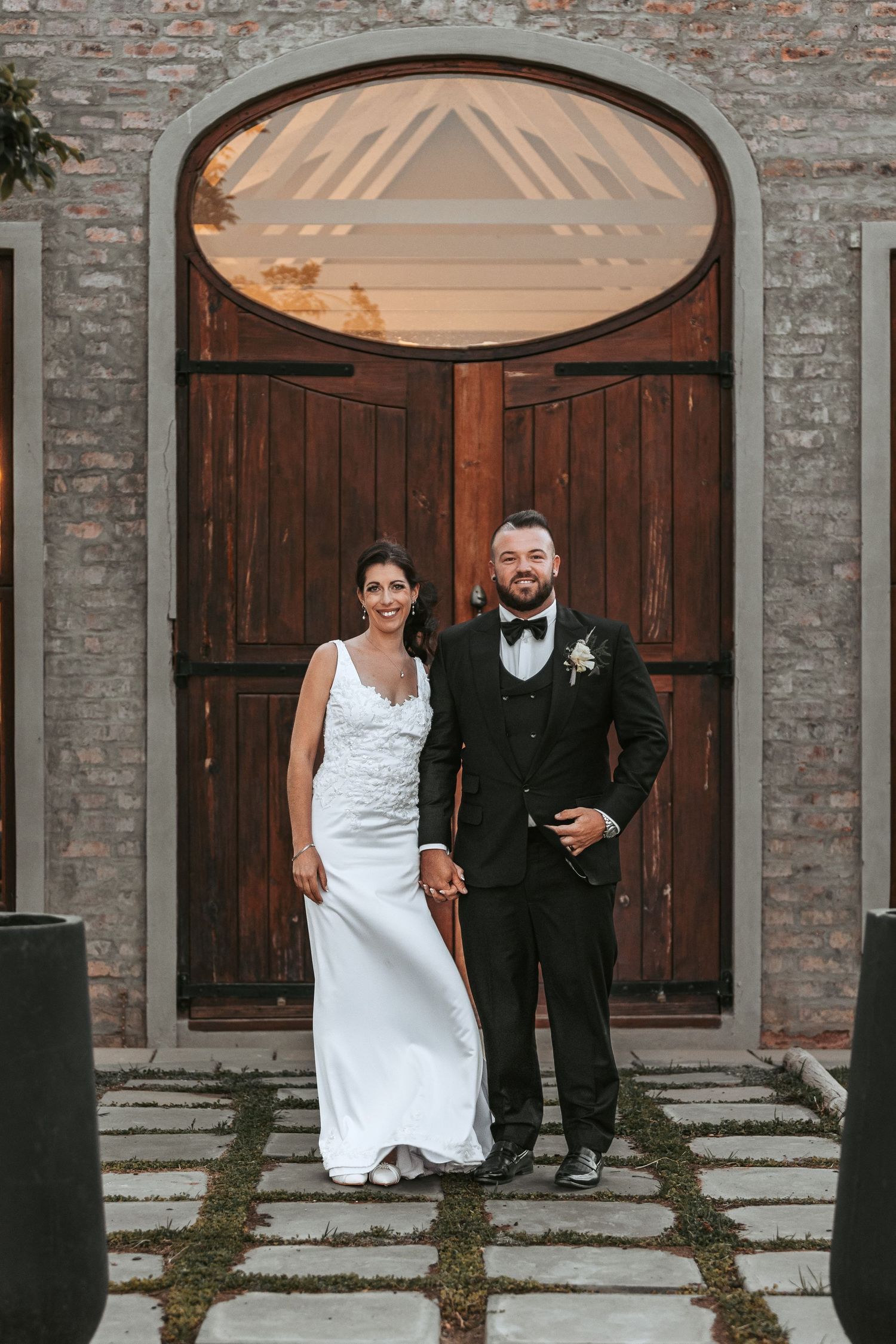 Wedding couple posing in front of rustic brick archways and wooden doors.