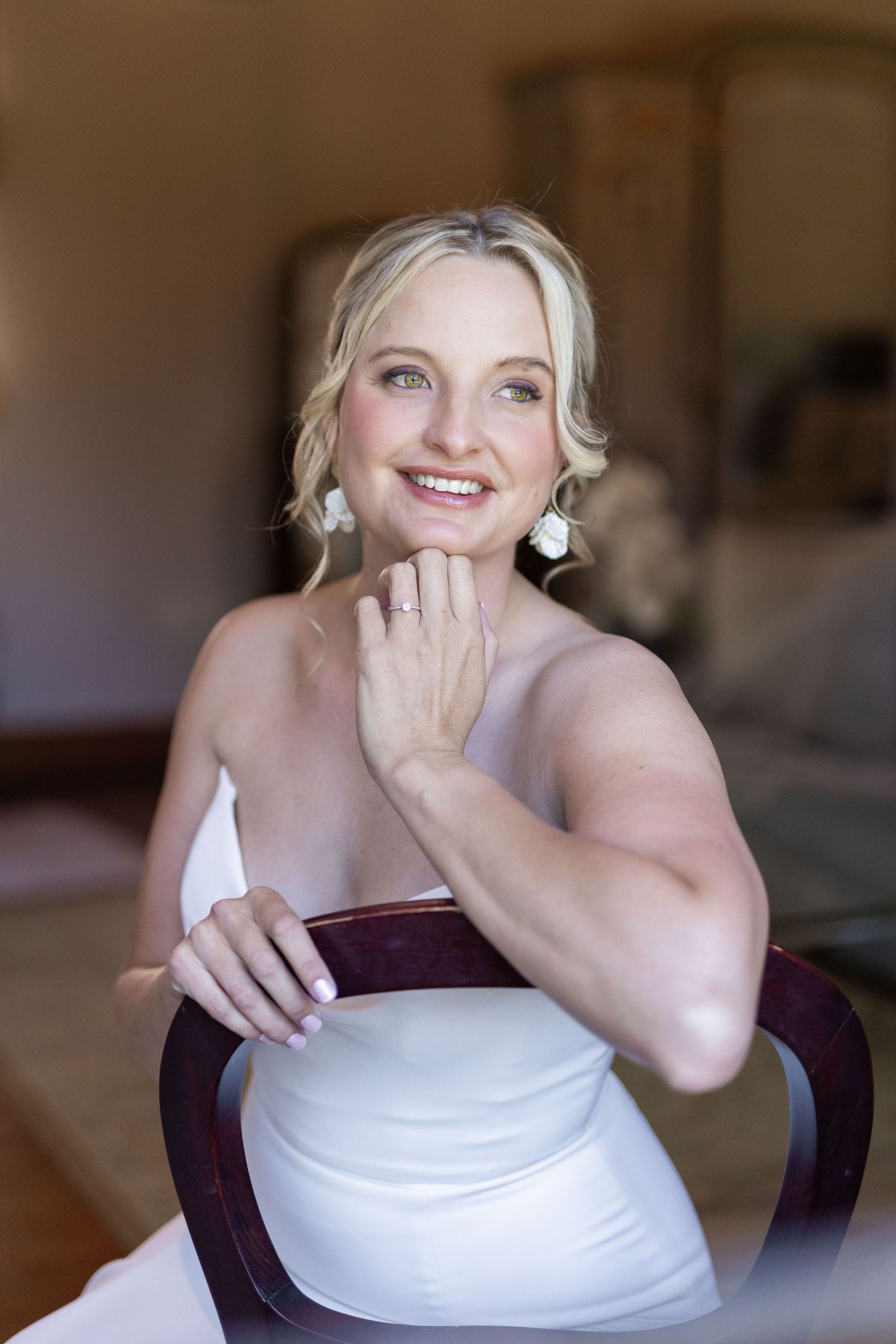 Bride in white dress sits elegantly in a chair while getting ready for her wedding day.