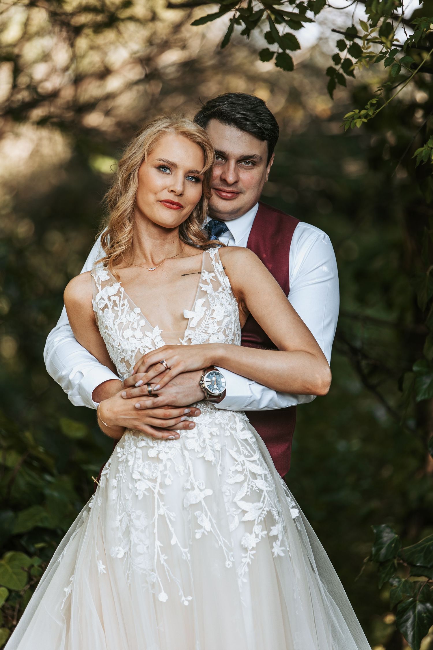 A couple embraces during their wedding photoshoot among trees and natural lighting.