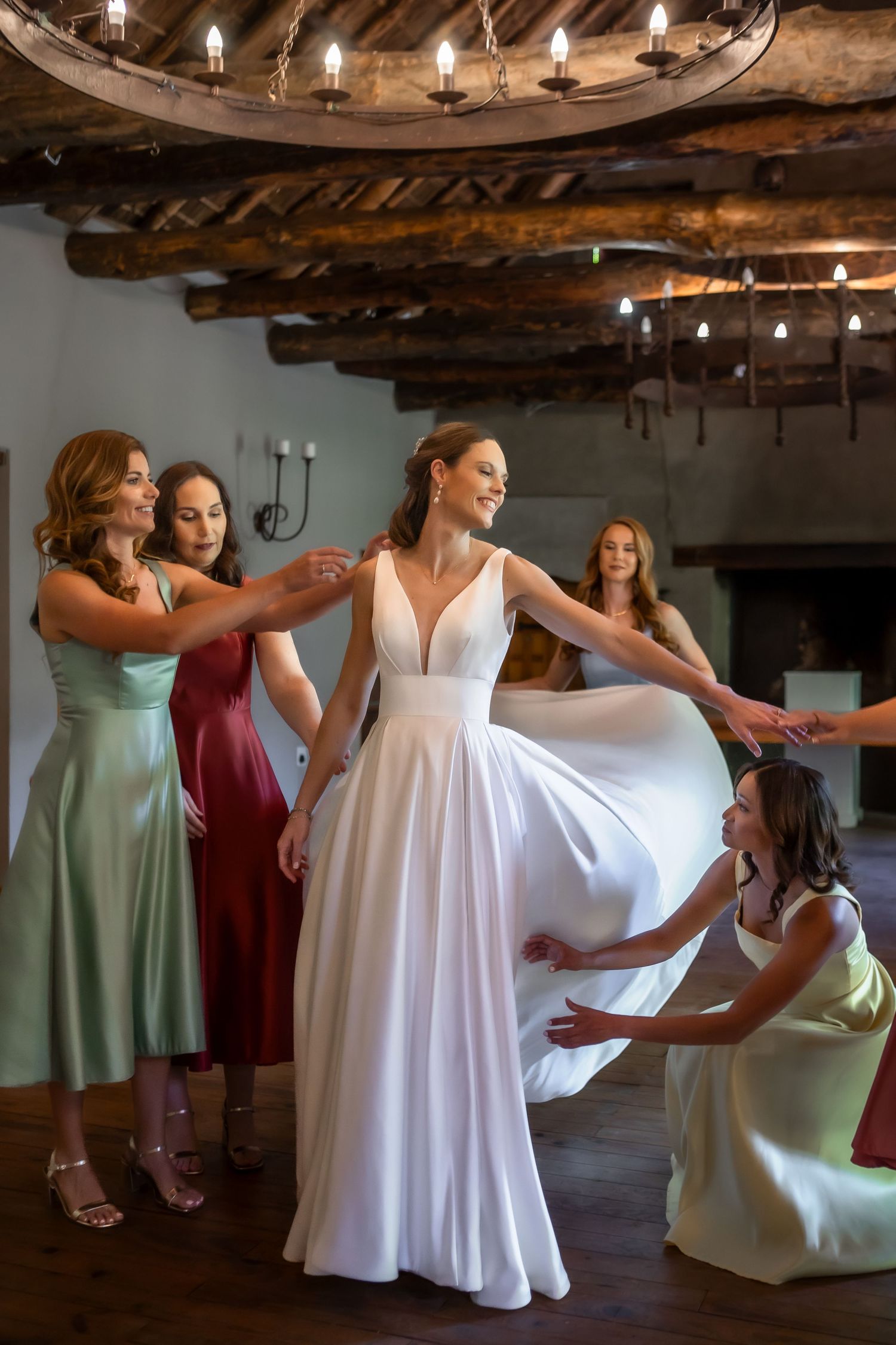 Bridesmaids help adjust the bride's white wedding dress in a rustic wooden beam venue.