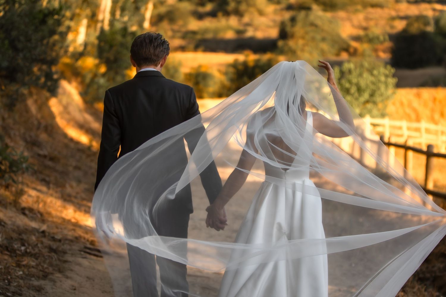 Romantic sunset wedding portrait with flowing veil creating ethereal silhouettes.