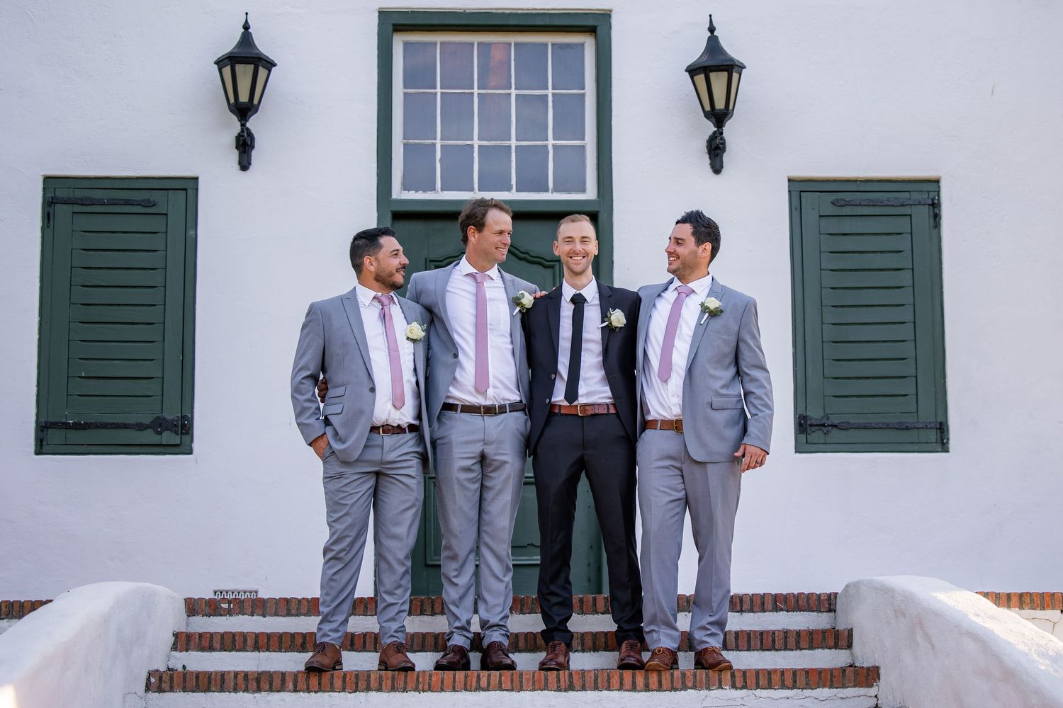 Wedding party in gray suits posing on white steps with green shutters and lanterns.