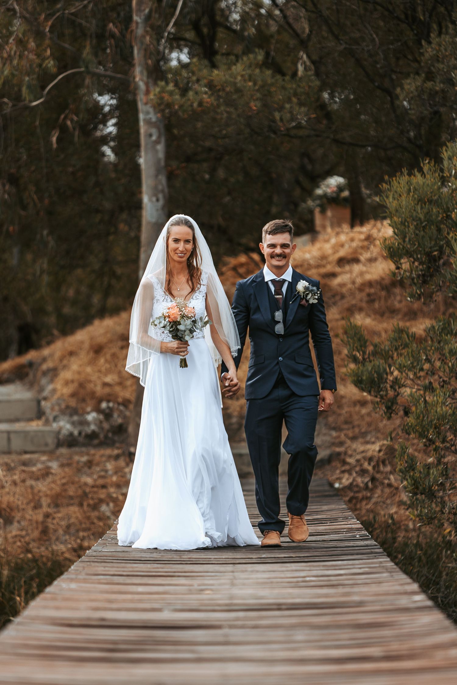 Couple walking along a wooden boardwalk during their wedding photoshoot.
