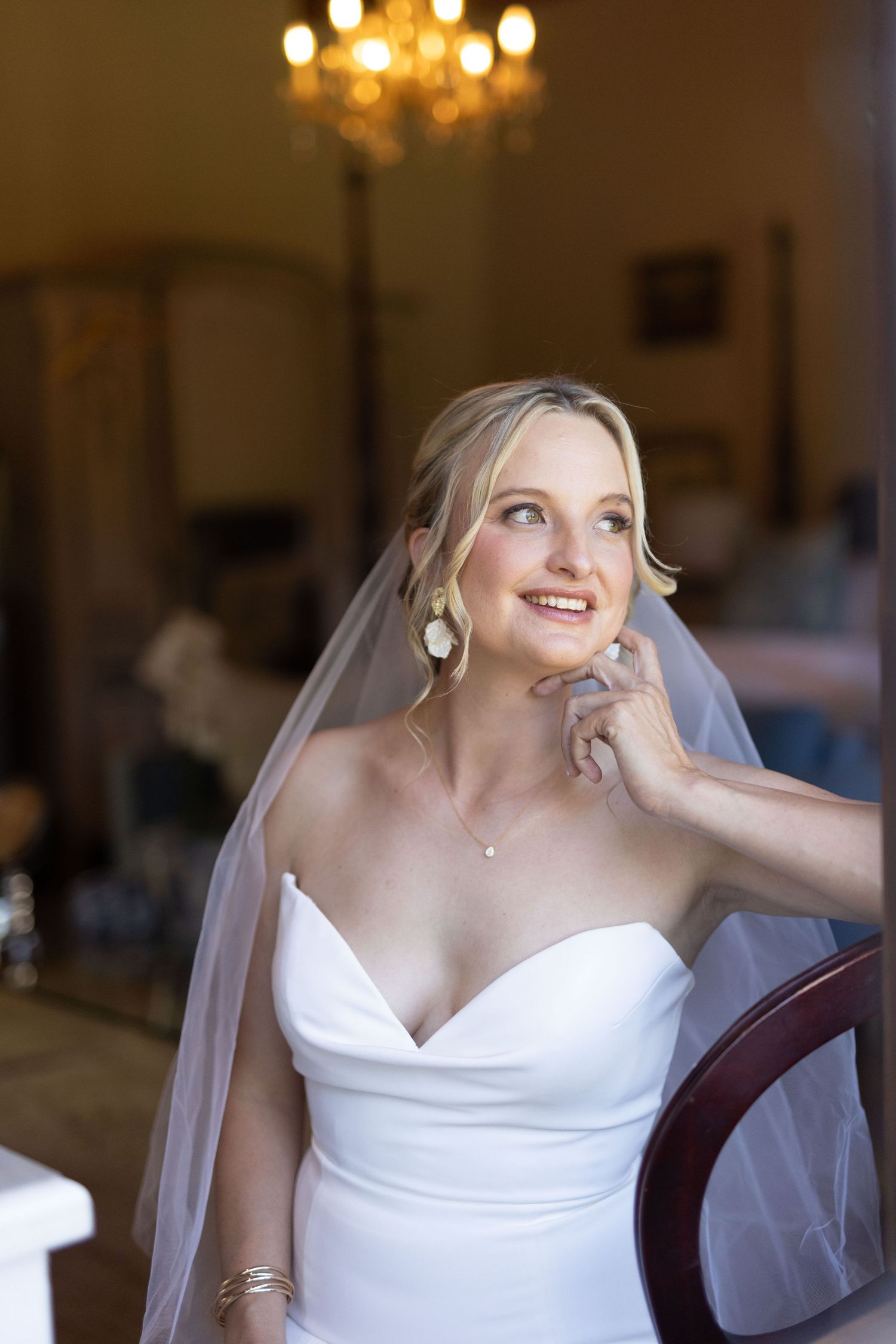 Bride in white wedding dress and veil poses gracefully in an elegant indoor setting.