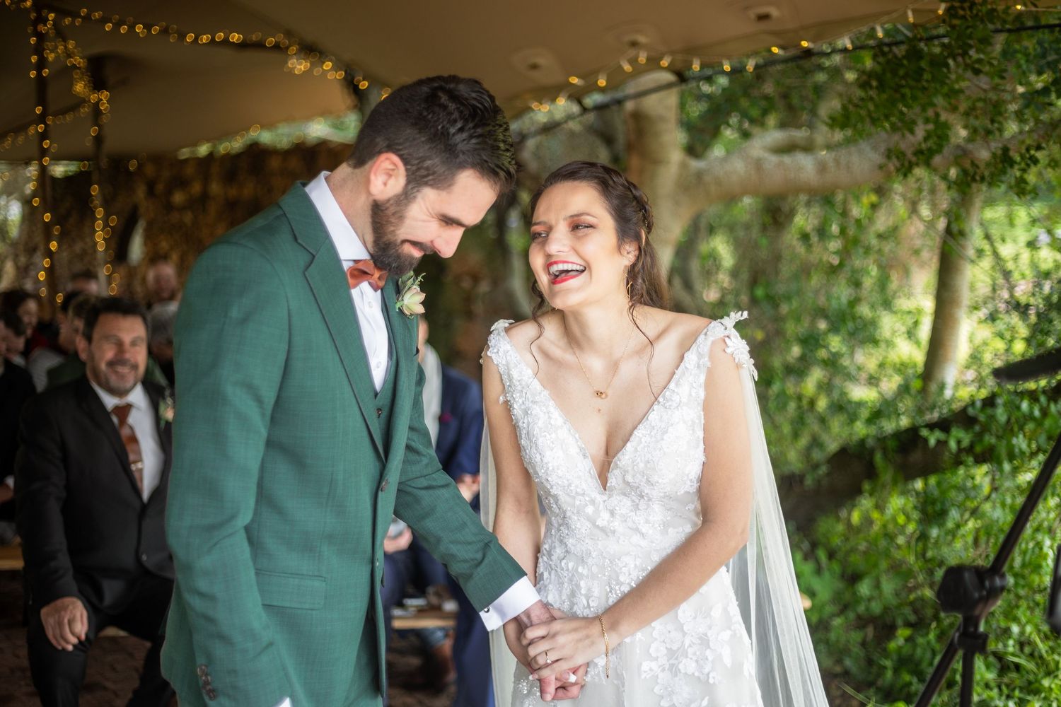 Couple in wedding attire sharing romantic moments in a garden setting with string lights and greenery.