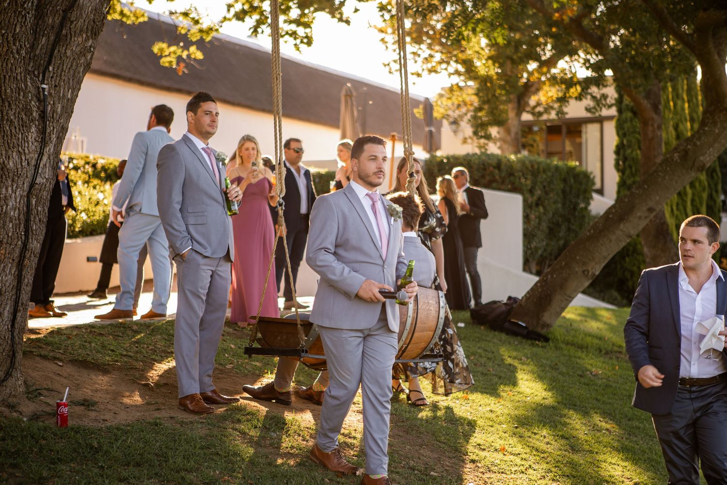 Guests gather outdoors during a sunset wedding celebration with golden light filtering through trees.