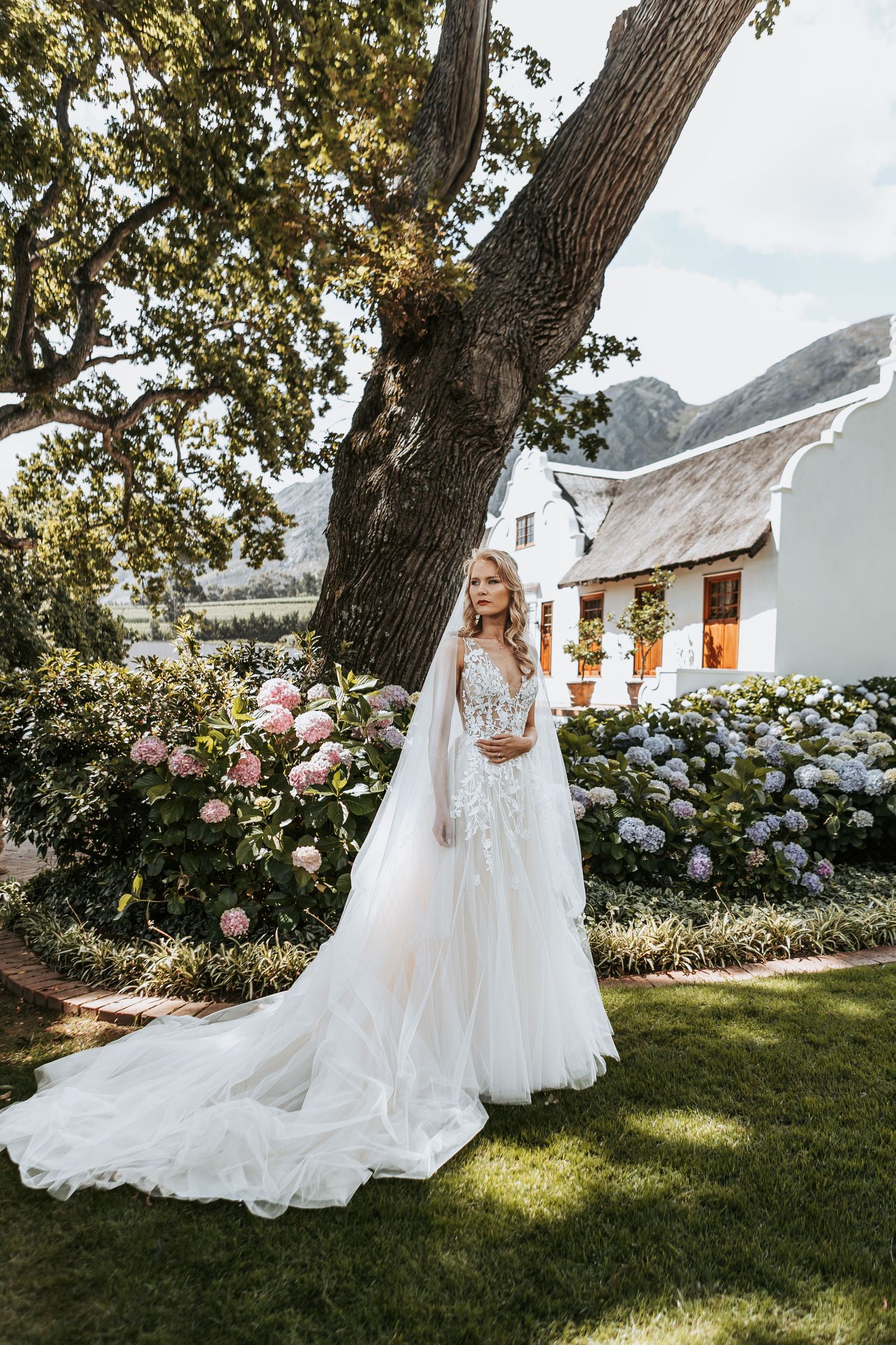 A flowing white wedding gown photographed in a garden setting with blooming roses and mountain views.