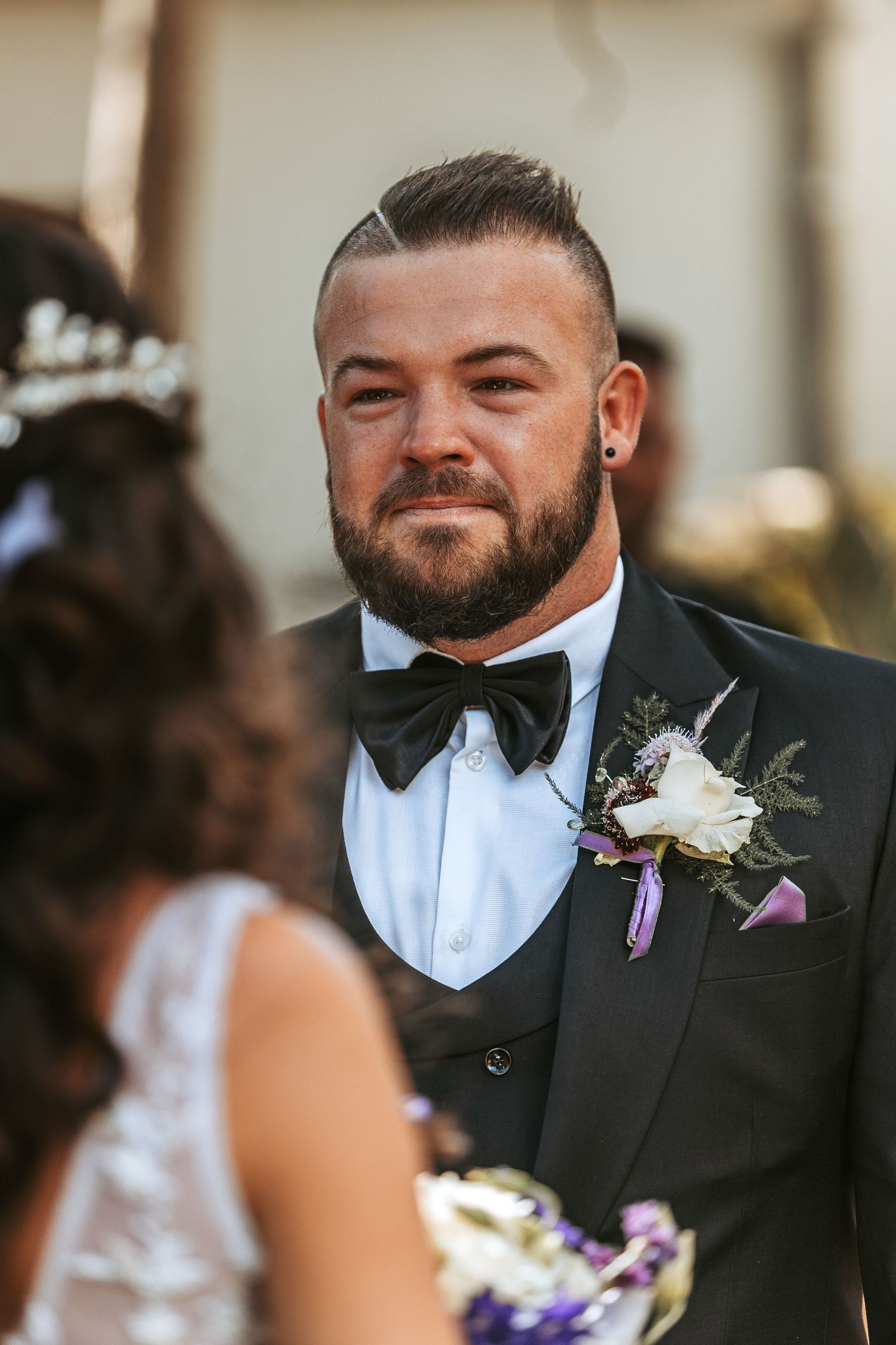 Emotional wedding ceremony moment with groom in black tuxedo and floral boutonniere.