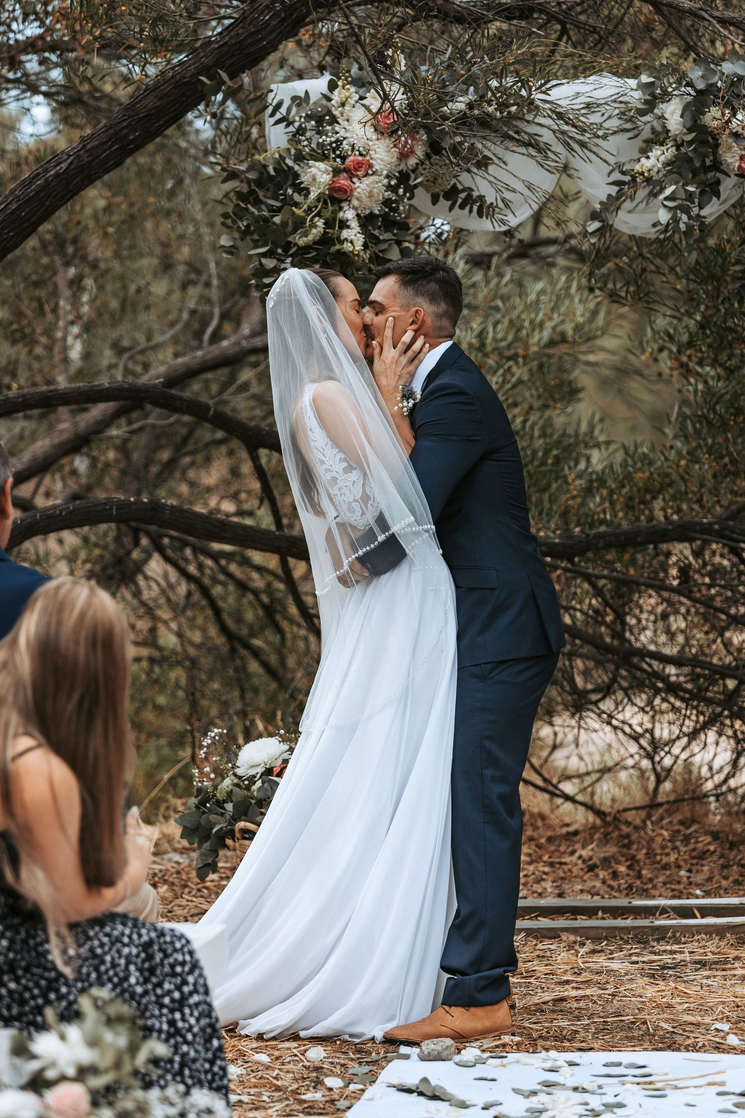 Romantic wedding moment captured under trees during an outdoor ceremony.