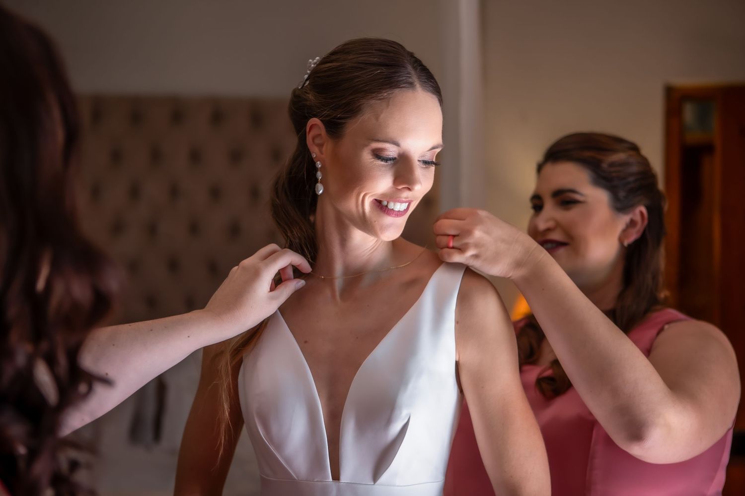 Wedding party members help with final dress preparations in a rustic venue.