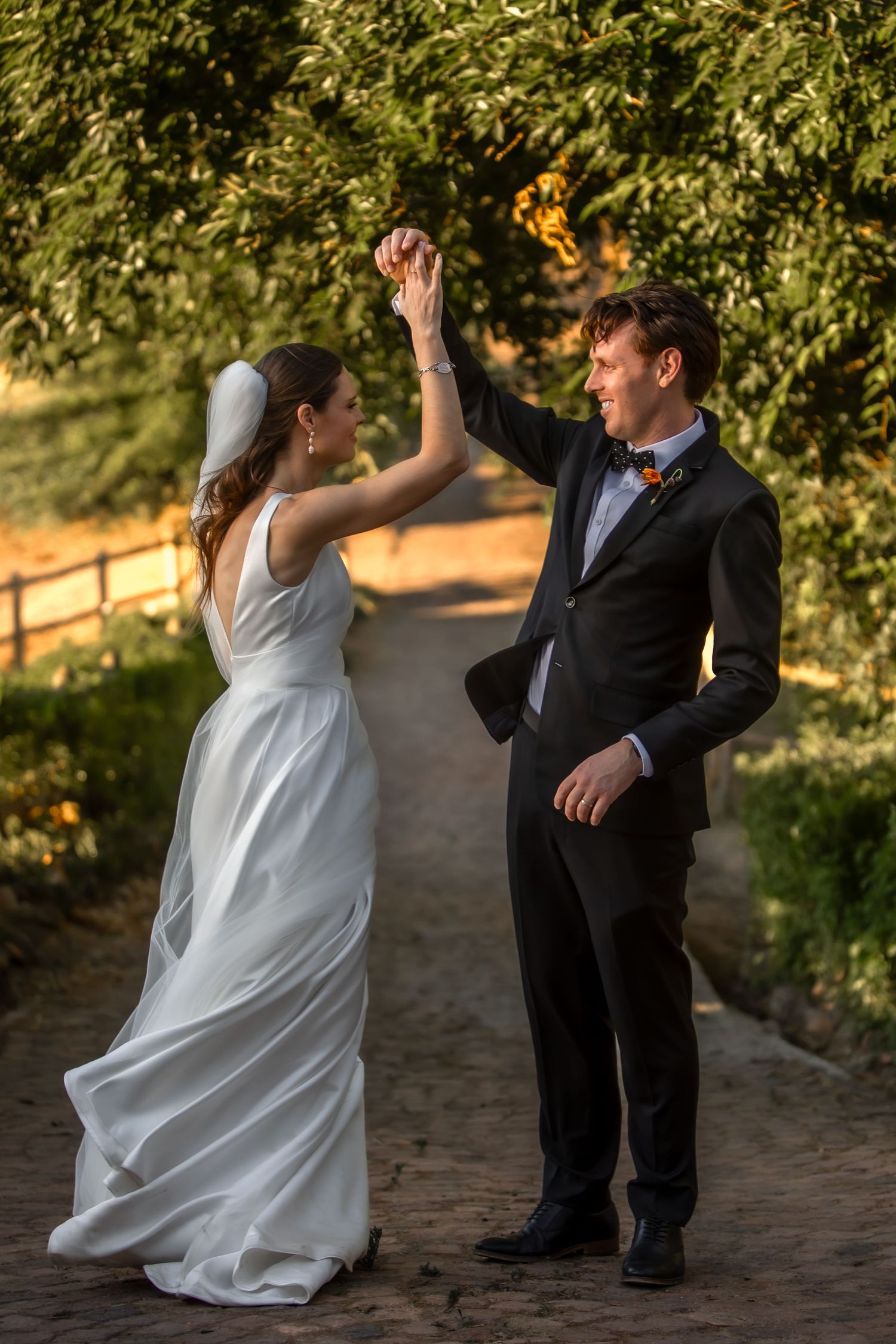 A joyful wedding couple high-fives on a garden path during sunset.