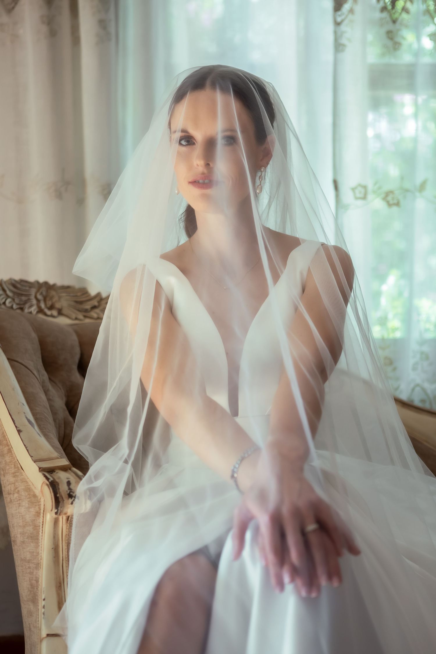 Artistic bridal photo with delicate veil draping creating dreamy atmosphere by window.