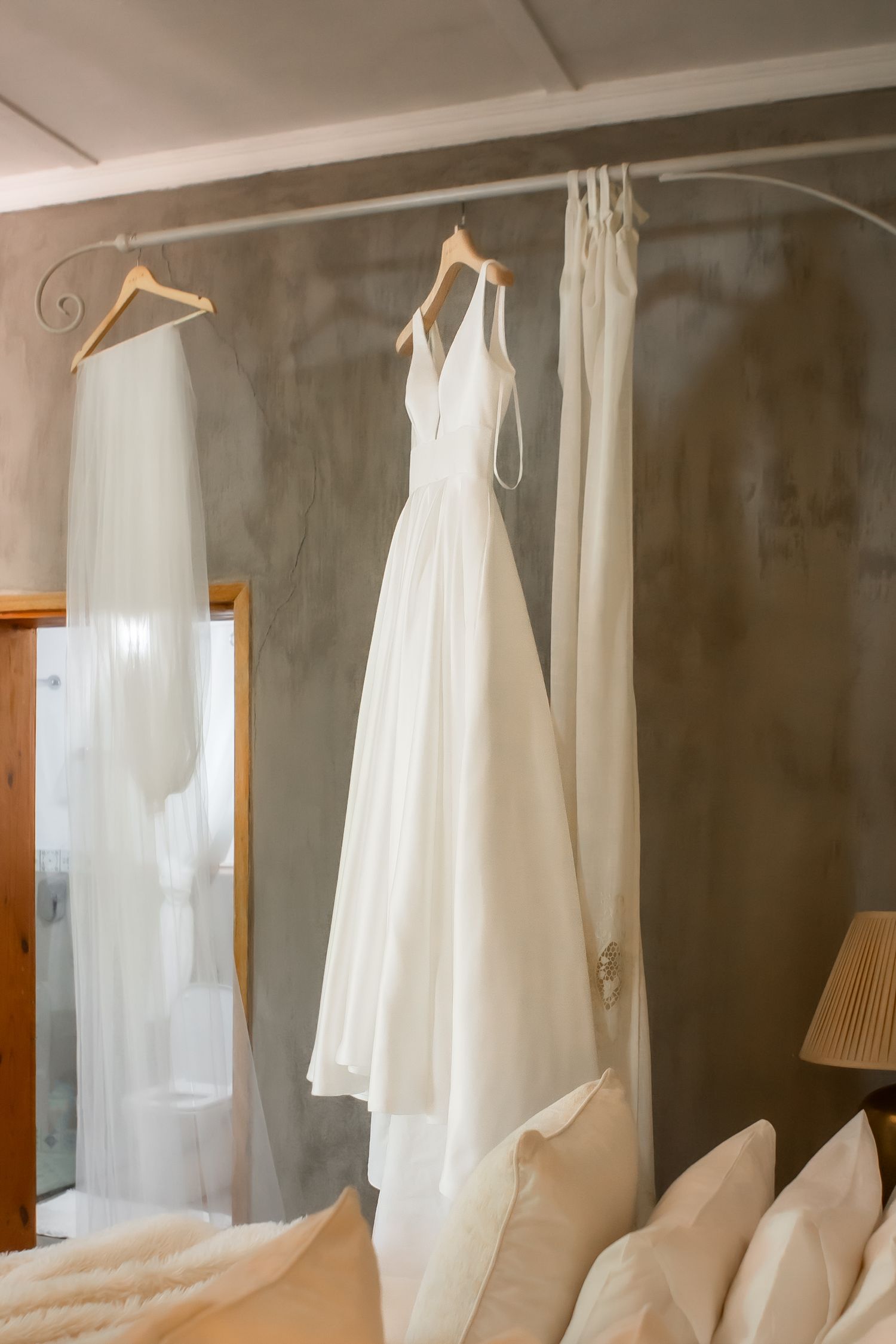 White bridal robes and dresses hanging on a rack against a gray wall.