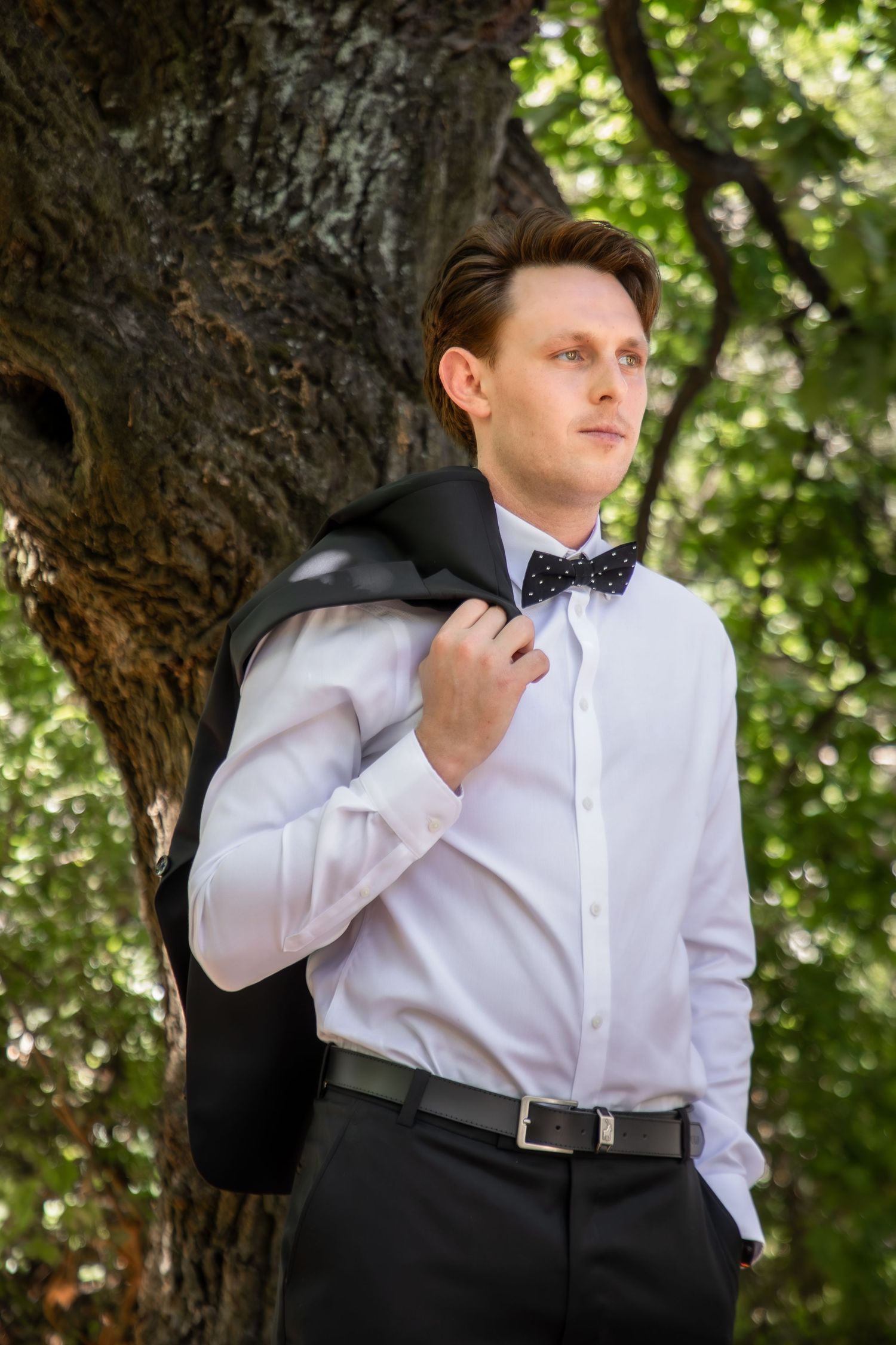 Formal attire and white shirt against a natural outdoor backdrop.