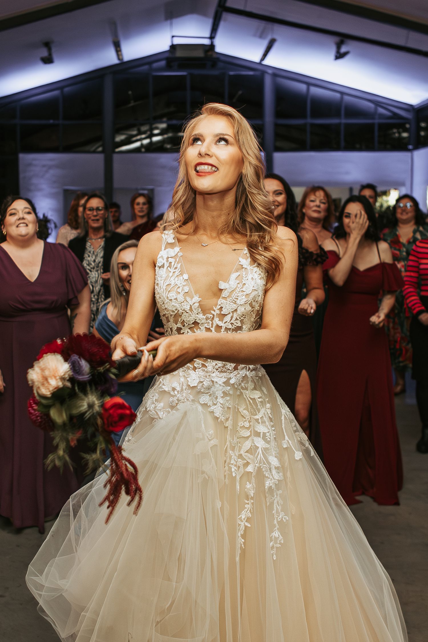 Joyful dance moments at a wedding reception with burgundy-dressed guests in the background.