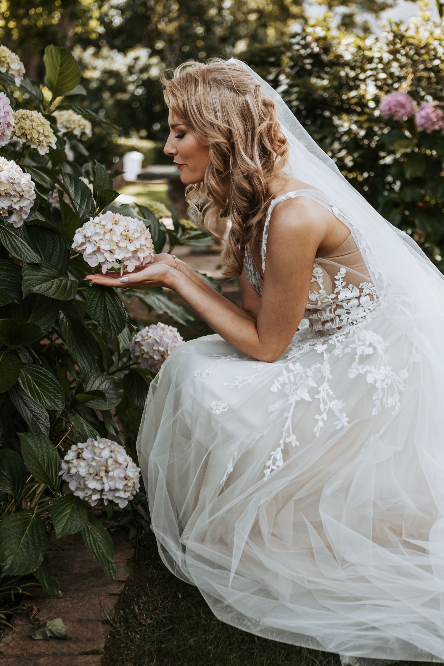A romantic wedding photo of a white lace gown among blooming hydrangea flowers in a garden setting.