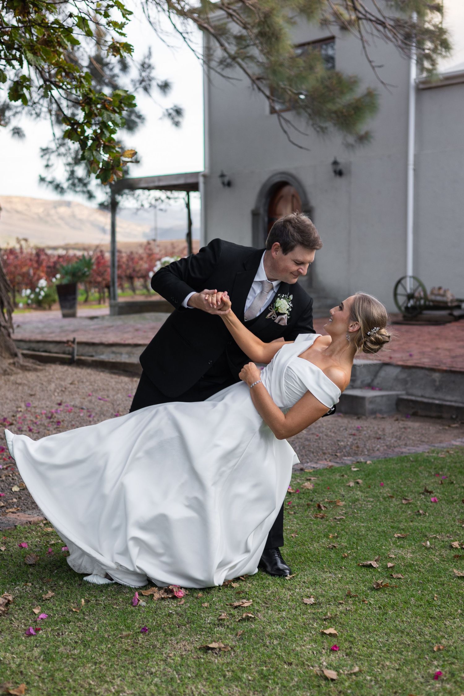 Groom dipping bride in white gown during romantic outdoor wedding photo session.
