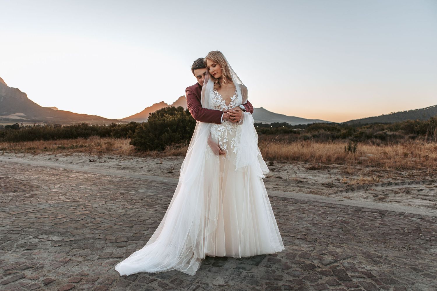 Newlyweds share romantic moment in desert setting during sunset photo session.