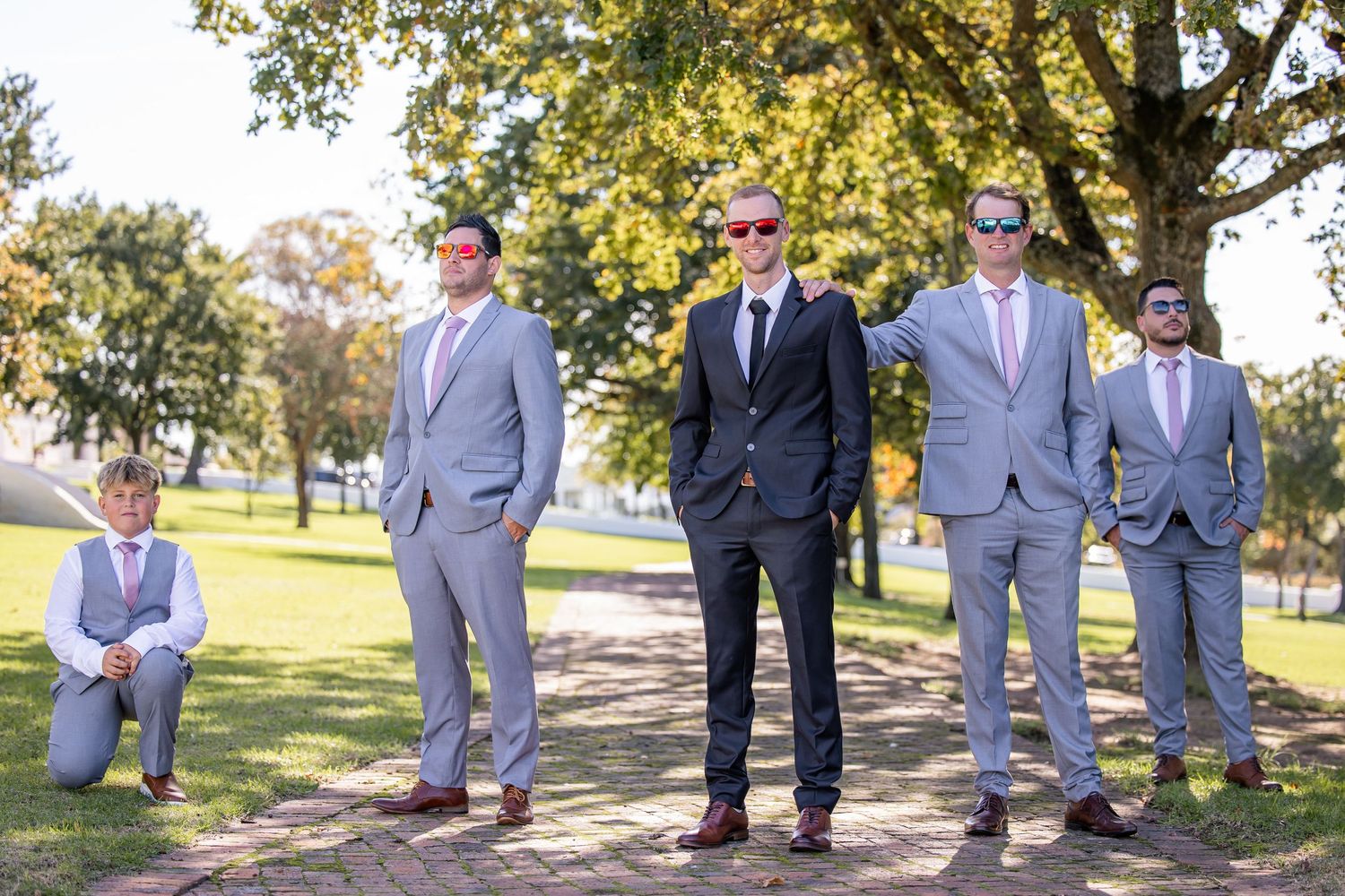 Wedding party in gray suits posing outdoors under autumn trees.