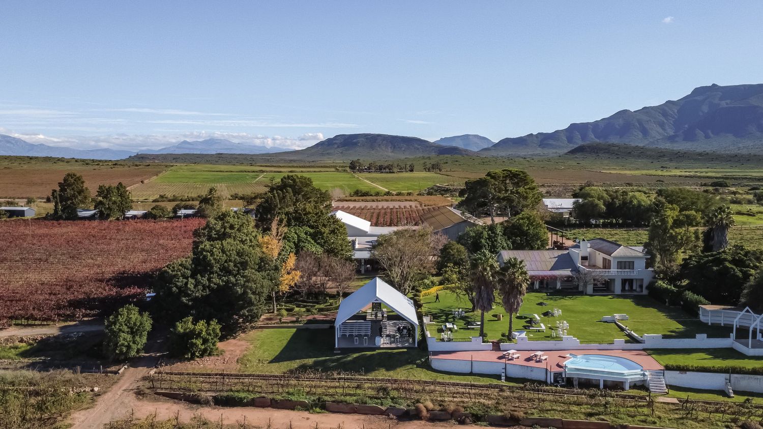 Aerial view of a scenic vineyard wedding venue with mountains and marquee tent.