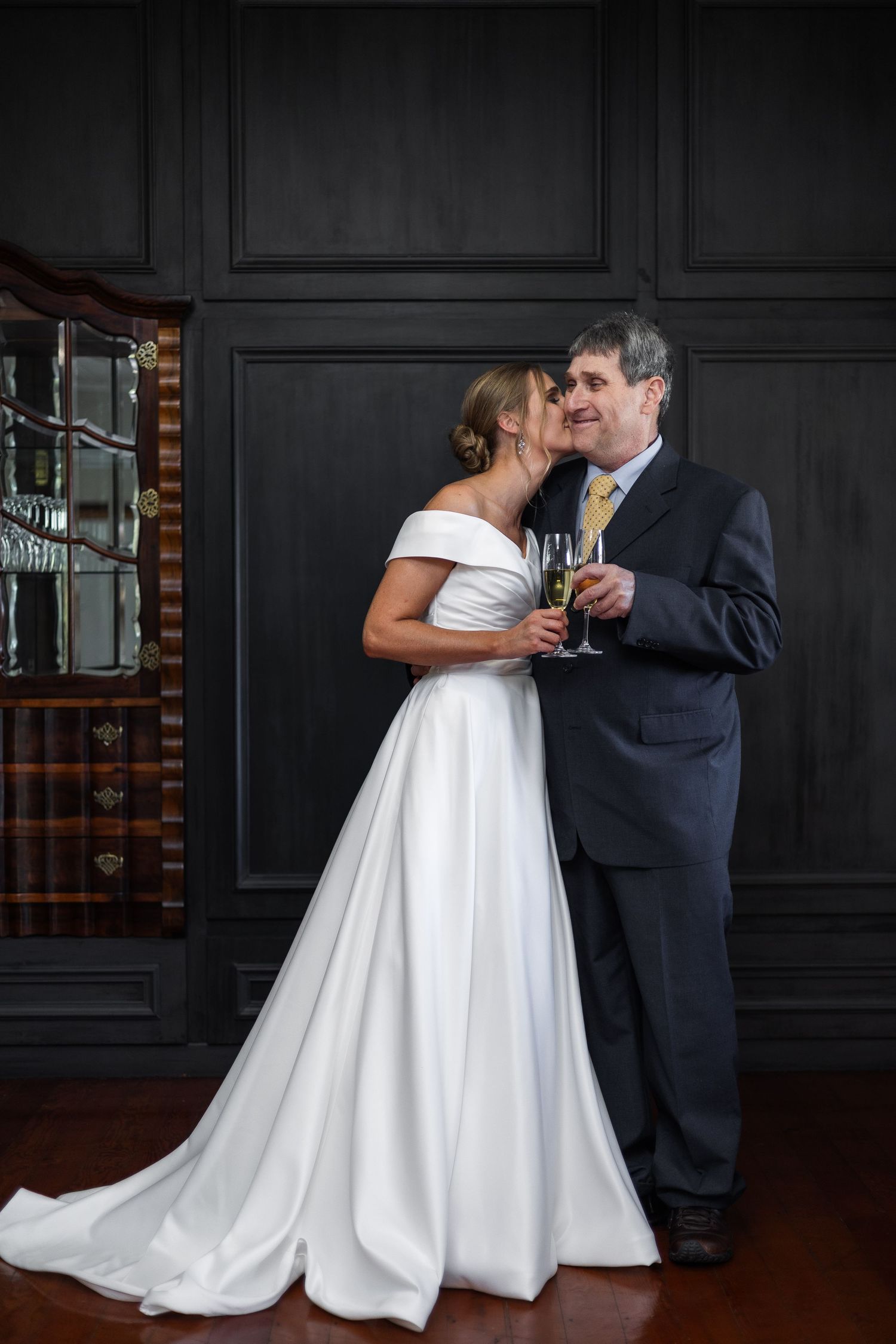 Bride and groom sharing a romantic moment with champagne glasses in an elegantly dark wood-paneled room.