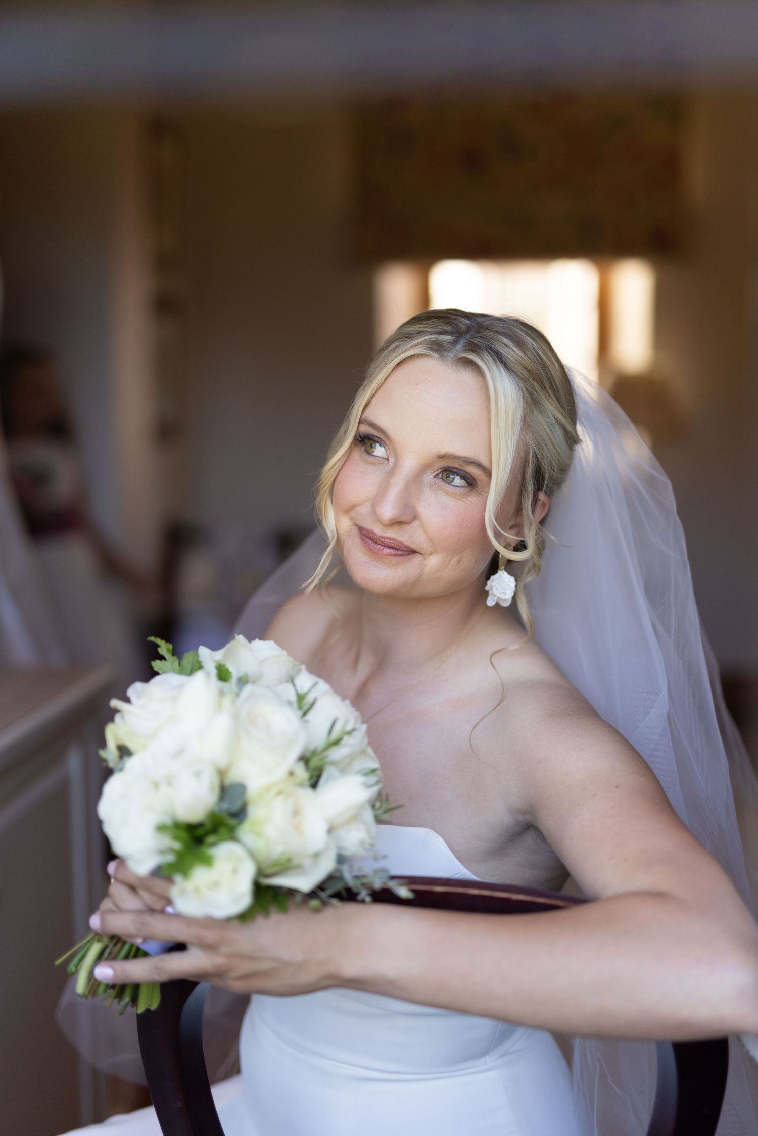 A bride in white holds her bouquet of white flowers while posing for portraits.