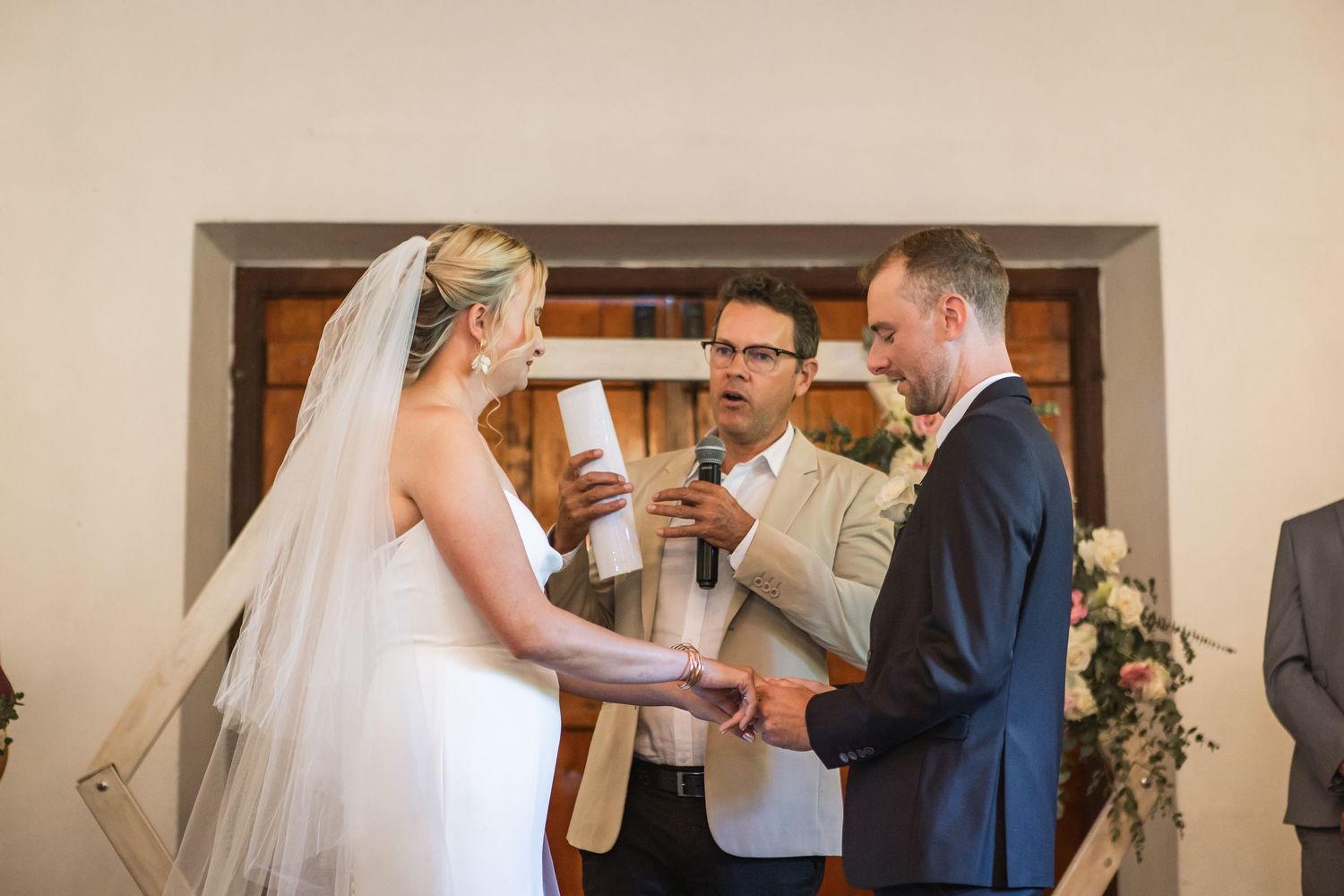 Wedding ceremony taking place in bright indoor venue with floral decorations.