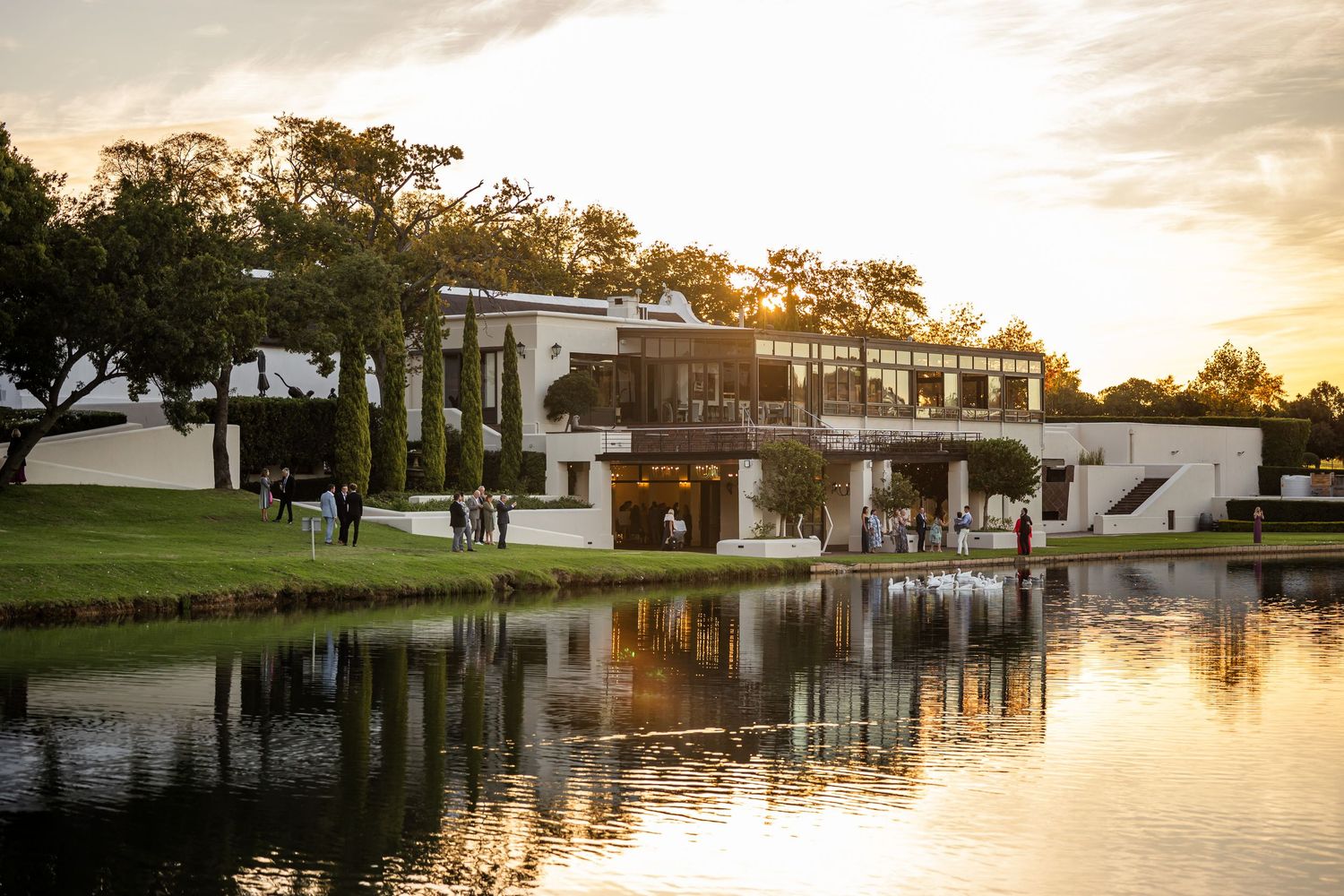 Waterfront venue reflects in calm lake waters during golden hour sunset.