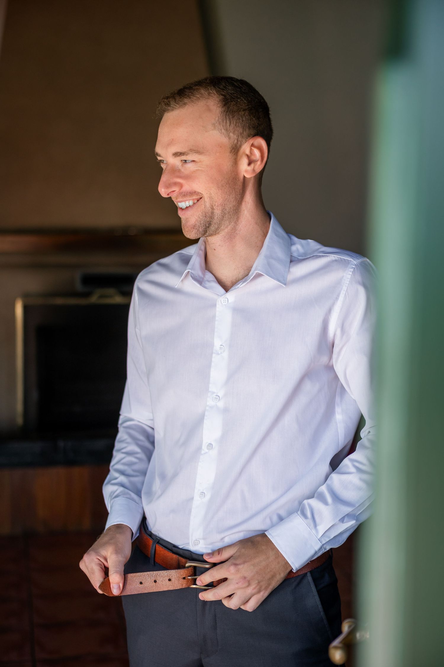 A groom getting ready on his wedding day, adjusting his tie while wearing a crisp white dress shirt.
