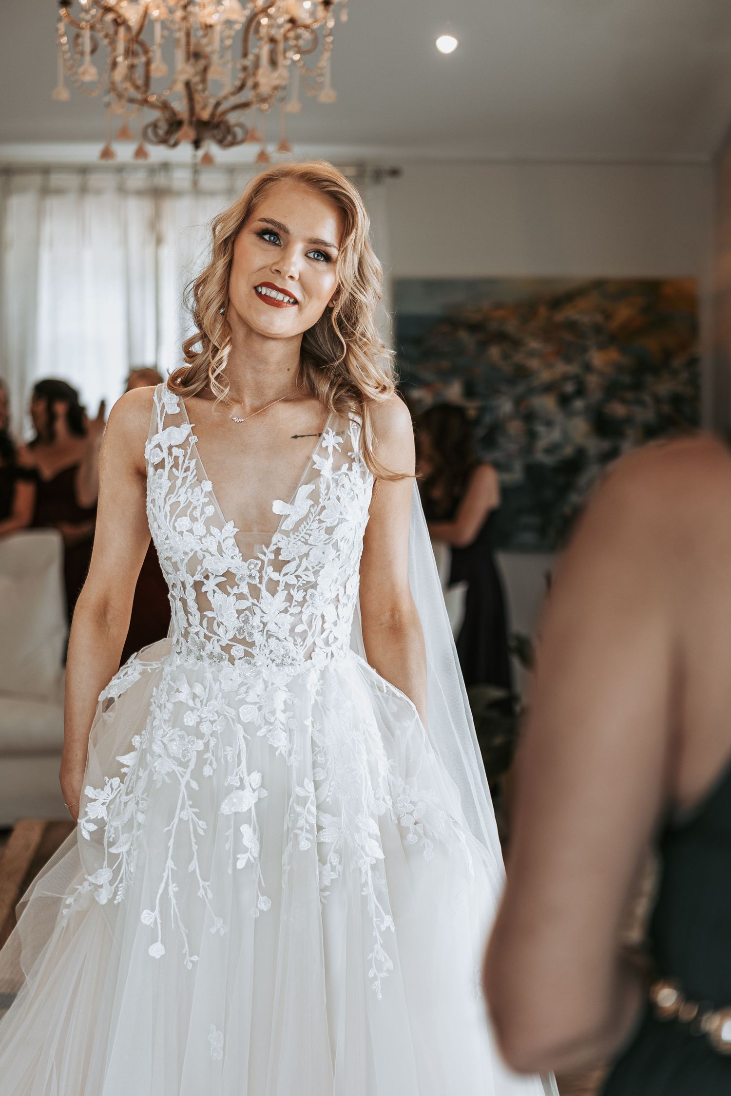 A beautiful white lace wedding dress with delicate floral appliques is displayed in an elegant room with chandeliers.