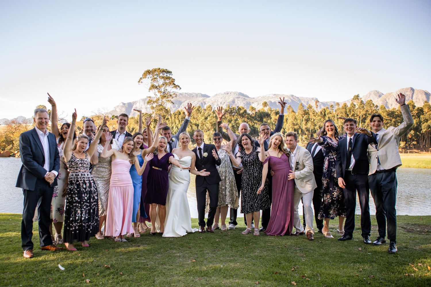 Large group wedding photo of guests and wedding party gathered outdoors at sunset.