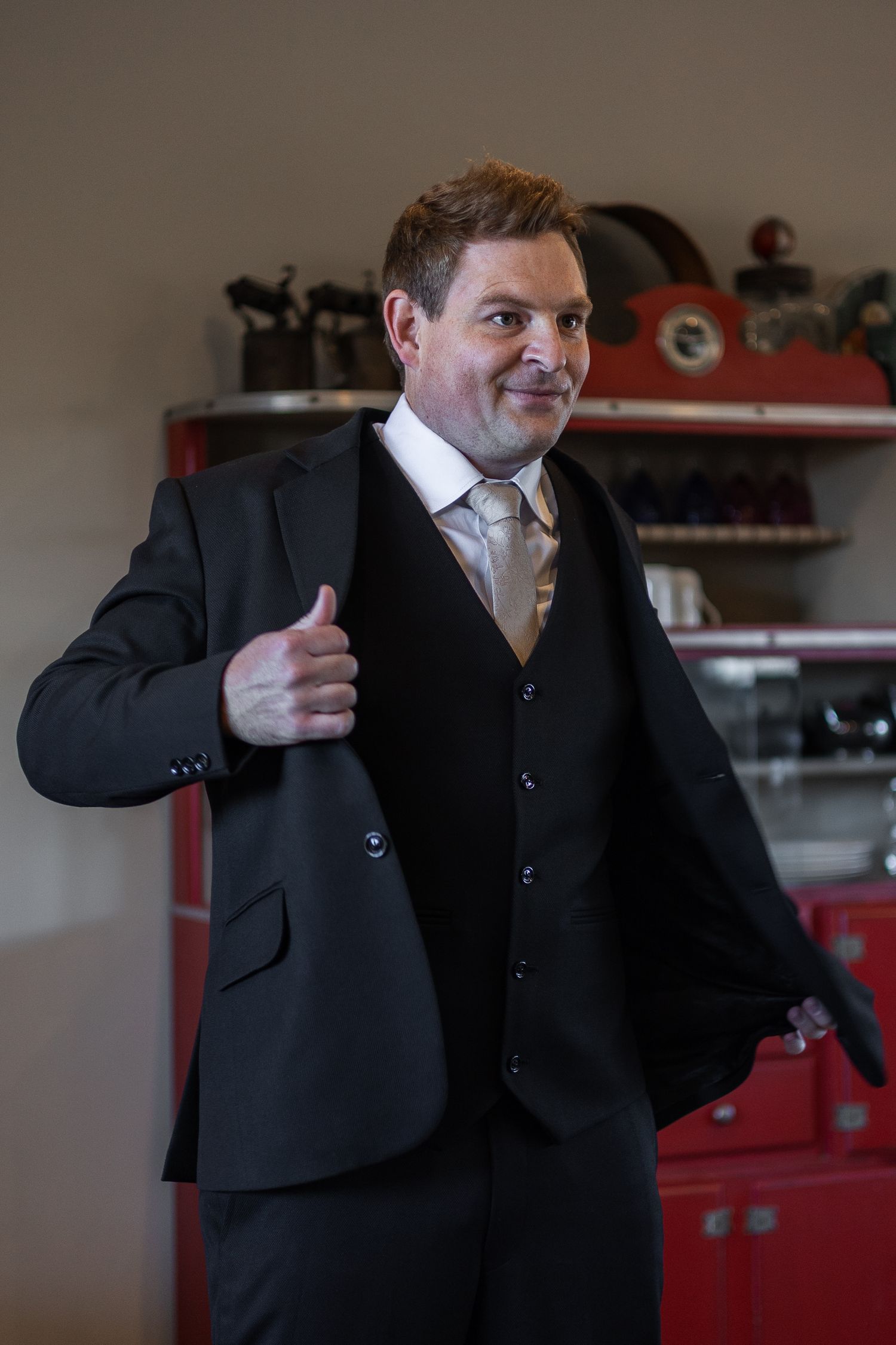Groom in black three-piece suit giving thumbs up while getting ready for wedding.