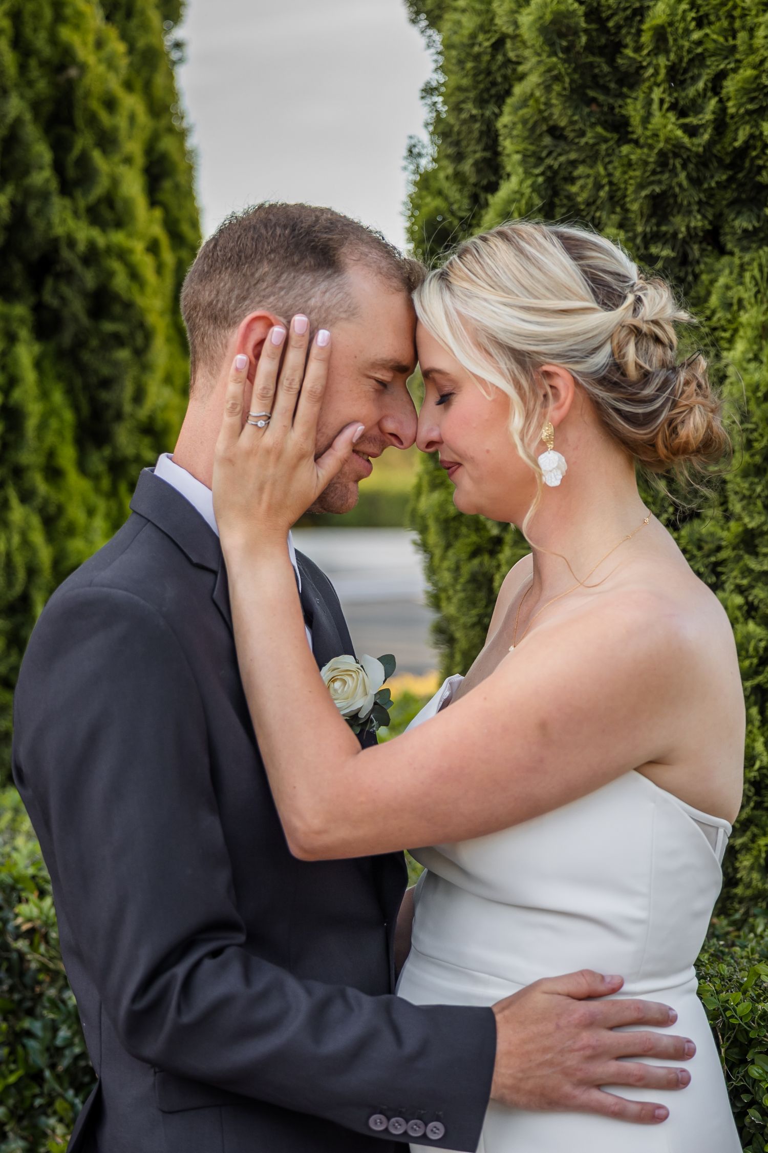 Romantic wedding couple shares intimate moments against a backdrop of lush green hedges.